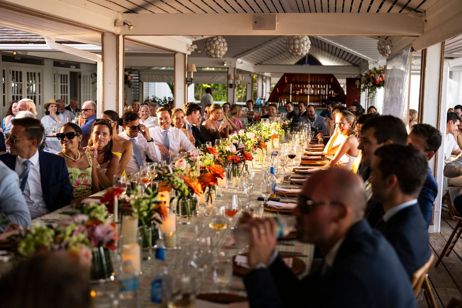 Elegant wedding reception dinner setup with long tables, floral centerpieces and warm lighting in a rustic venue.