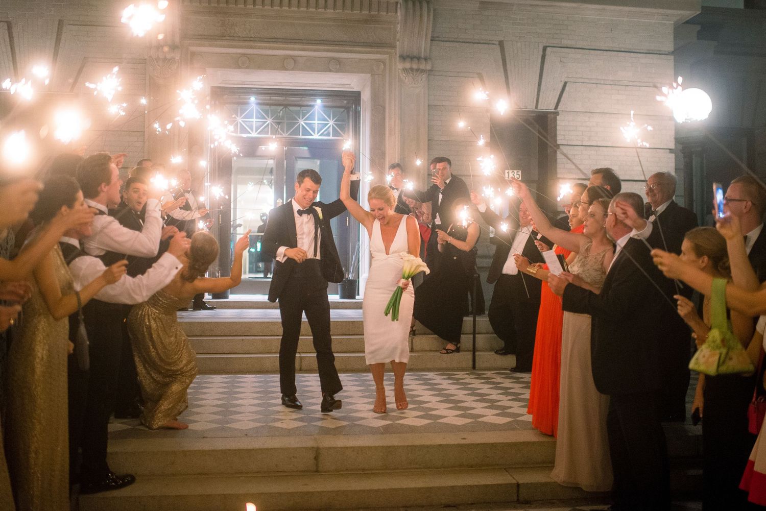 Wedding guests hold sparklers creating a glowing tunnel for the newlyweds to walk through during their reception exit.