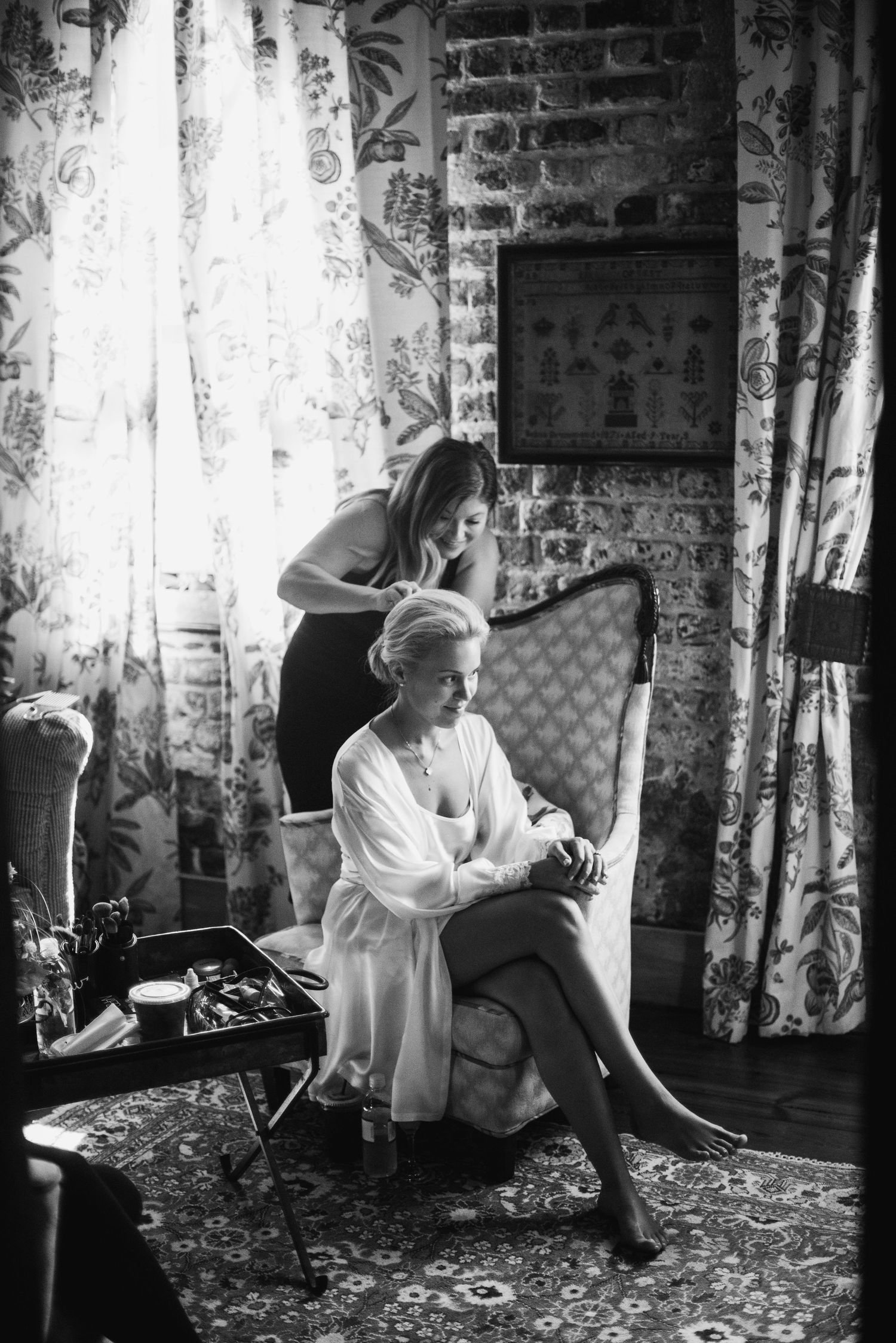 Black and white photo series showing a person in a white outfit sitting in a cluttered vintage room with floral curtains.