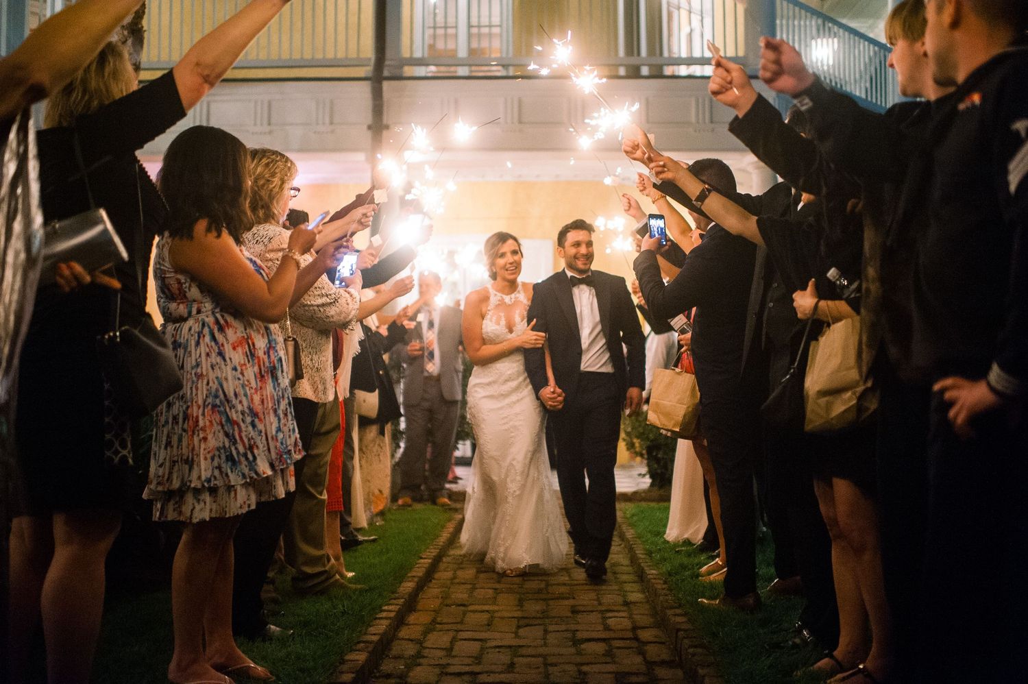 Wedding guests form a sparkler tunnel at night creating a magical illuminated pathway.