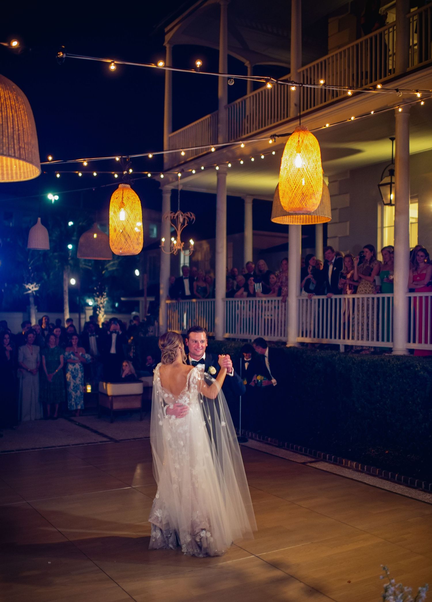 A couple shares their first dance under warm string lights at a romantic outdoor wedding reception.