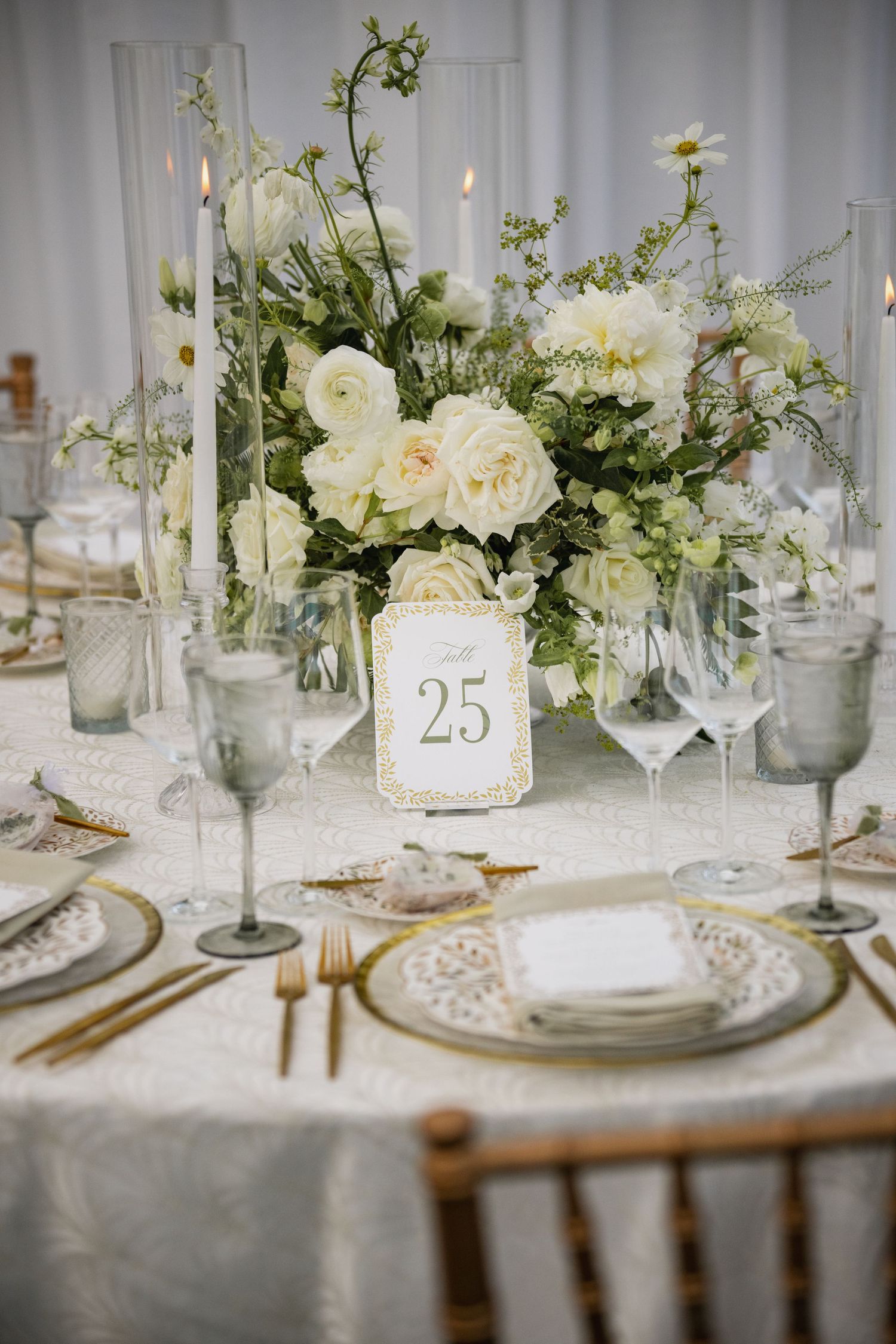 Luxurious wedding table setting with white floral centerpieces, crystal glassware, and gold accents.