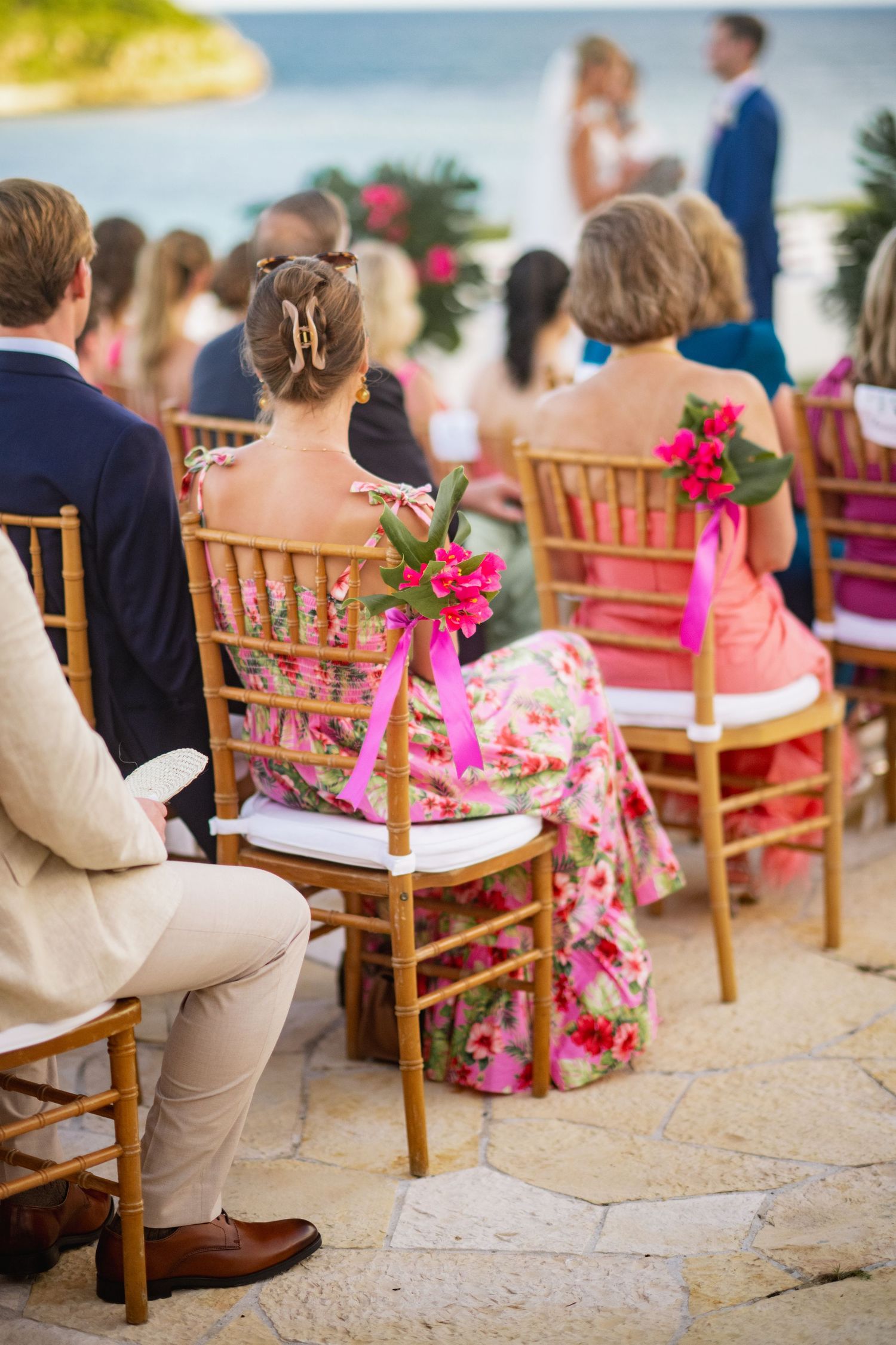 Wedding ceremony seating with wooden chairs decorated with pink flowers by the ocean.