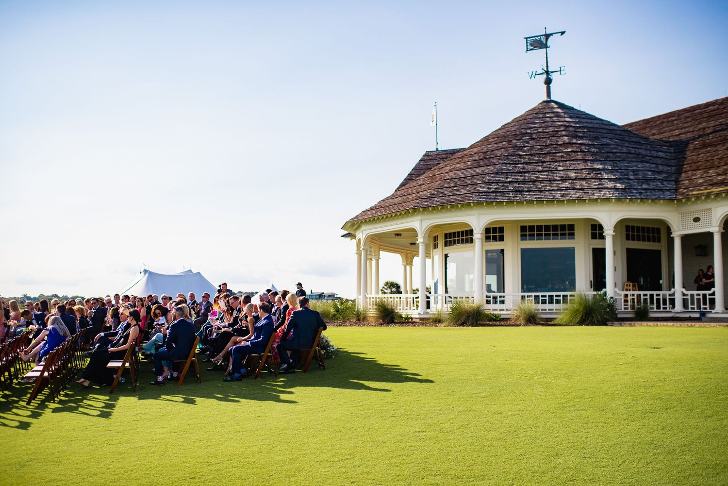 Panoramic view of a wedding ceremony at a hilltop venue with a white gazebo and guests seated outdoors.