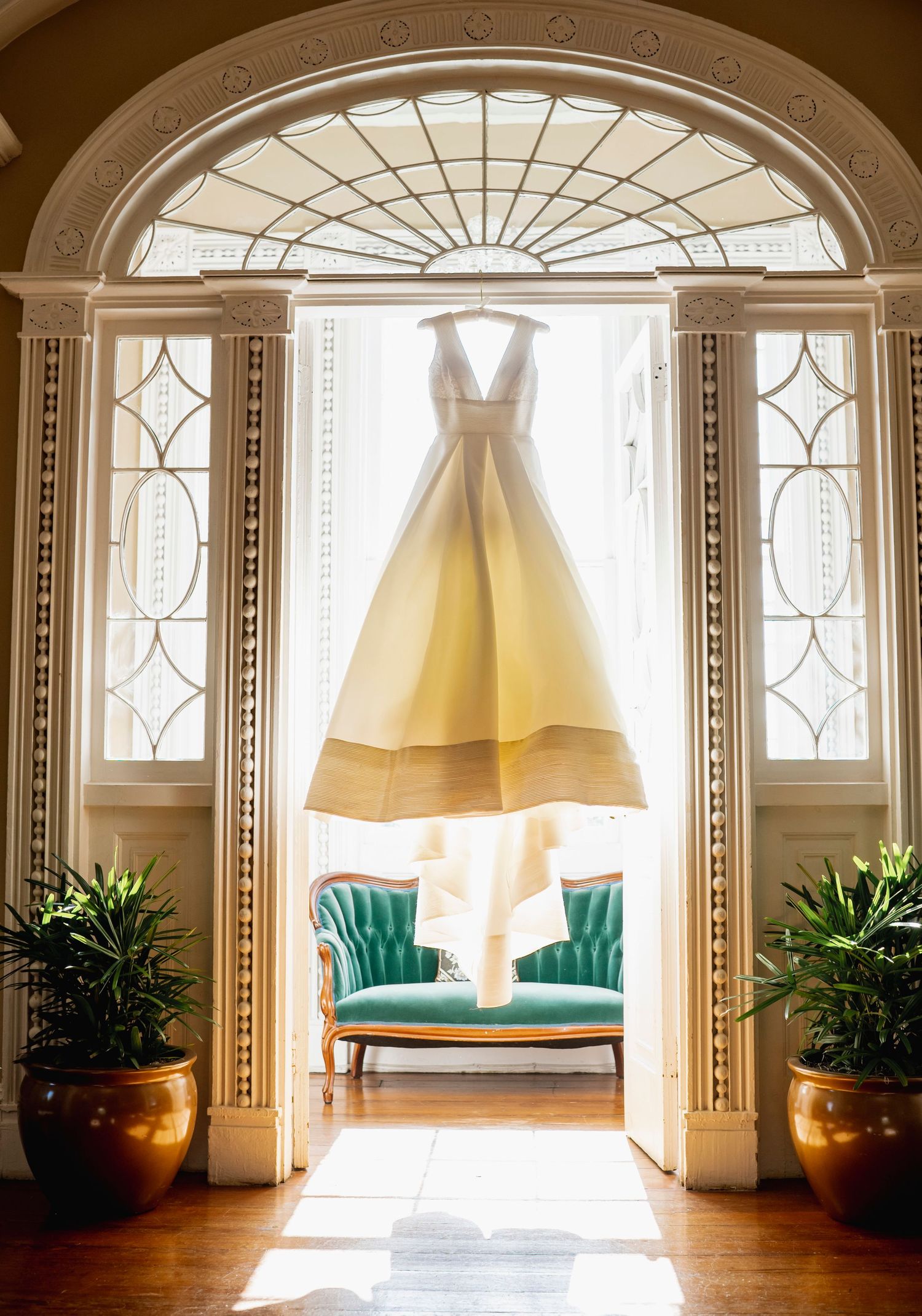 Wedding dress hanging in elegant arched doorway with natural light streaming through leaded glass windows.