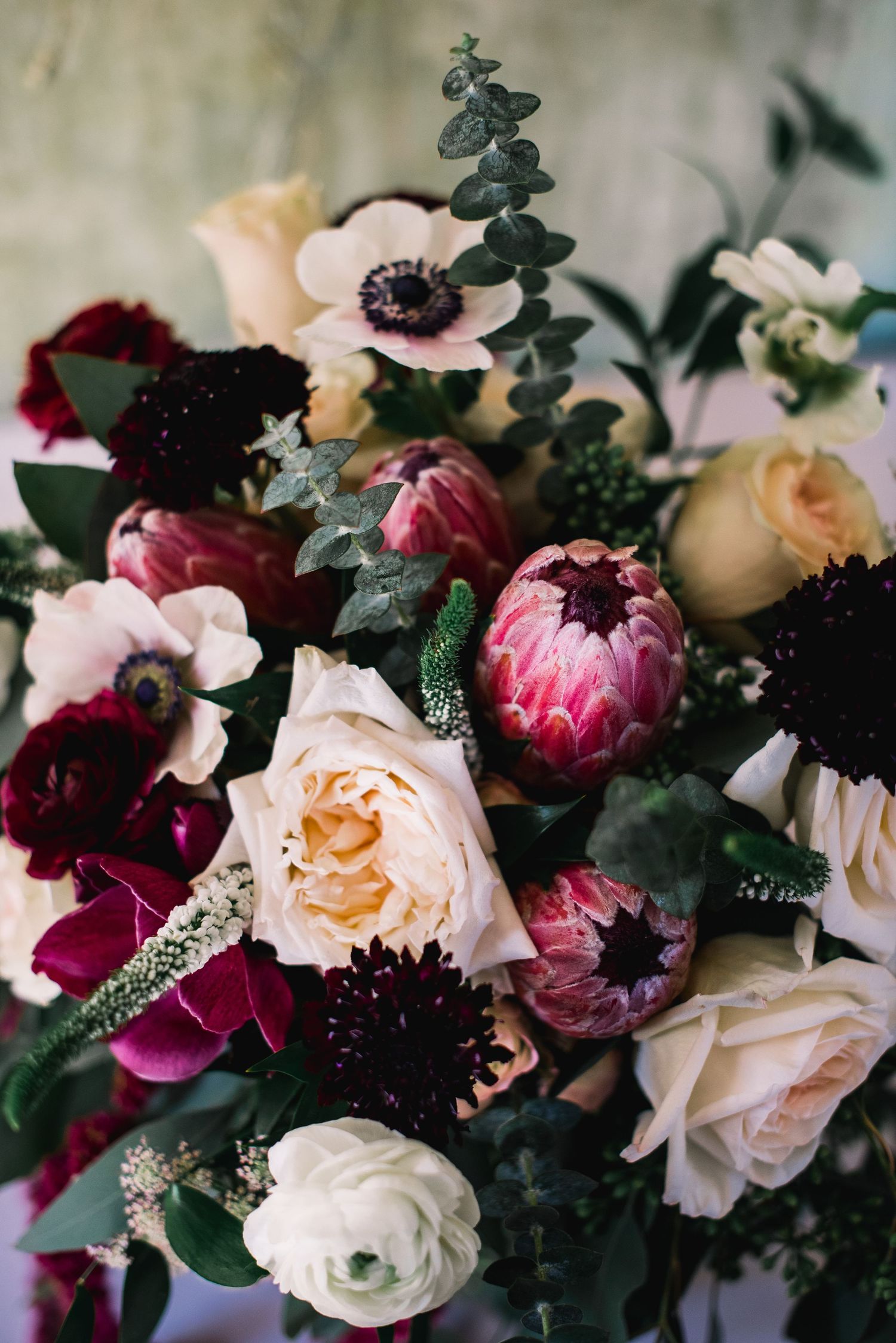Romantic floral arrangement featuring blush roses, deep burgundy blooms, and dark green foliage in moody lighting.