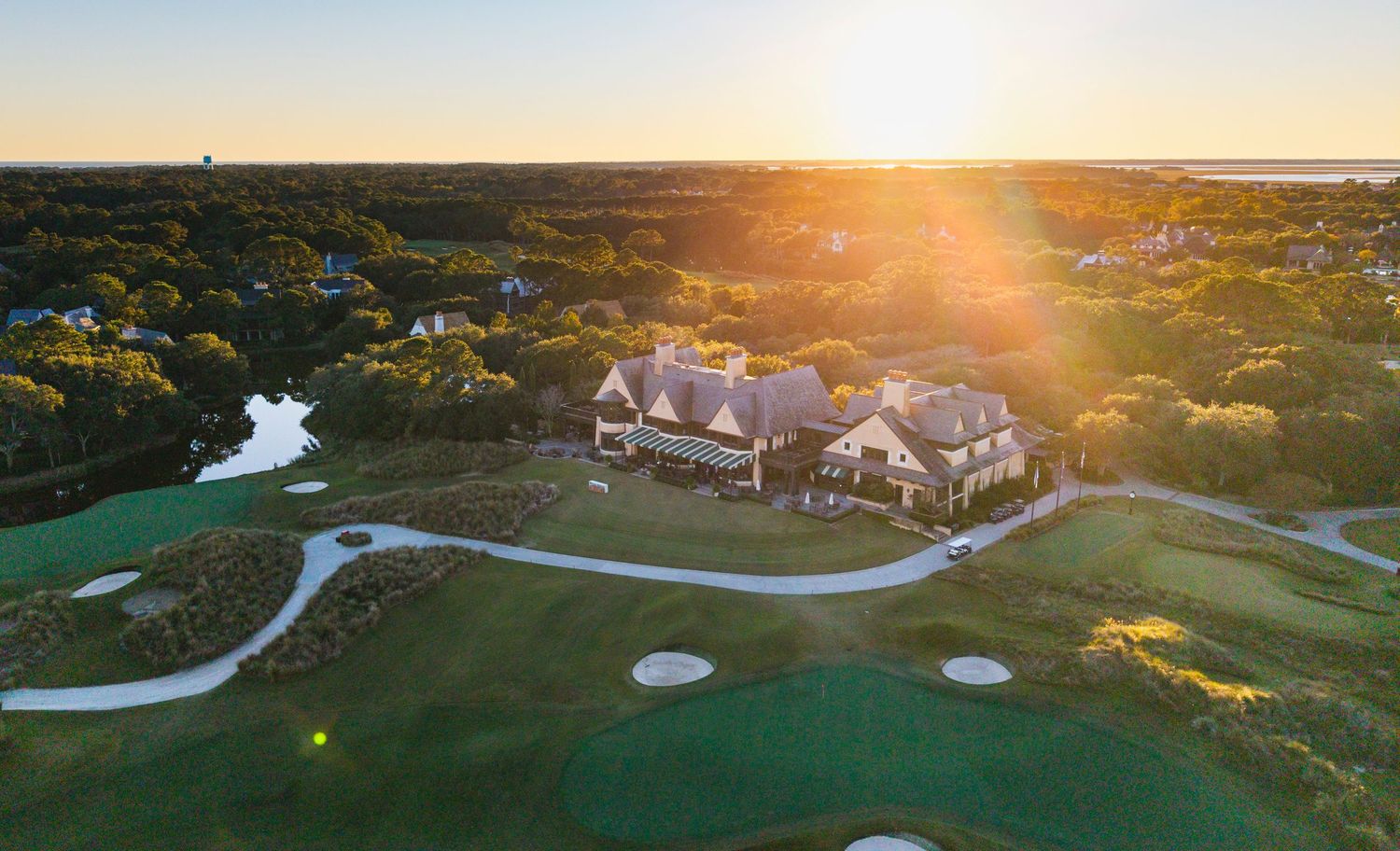 Aerial panoramic view of a golf course with winding paths and sand bunkers at golden sunset.