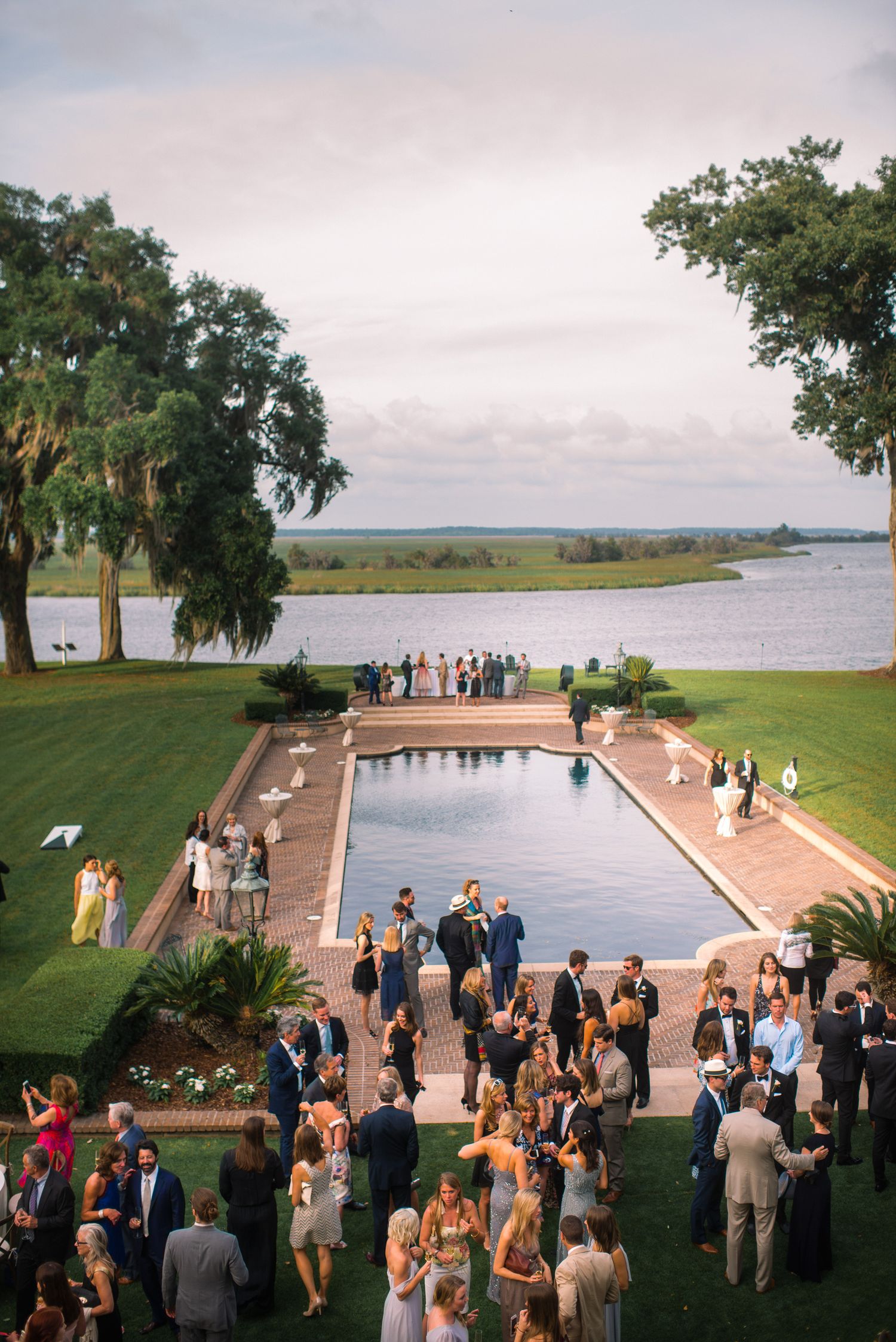 Guests gather at a waterfront venue overlooking a serene lake during an elegant outdoor event at sunset.