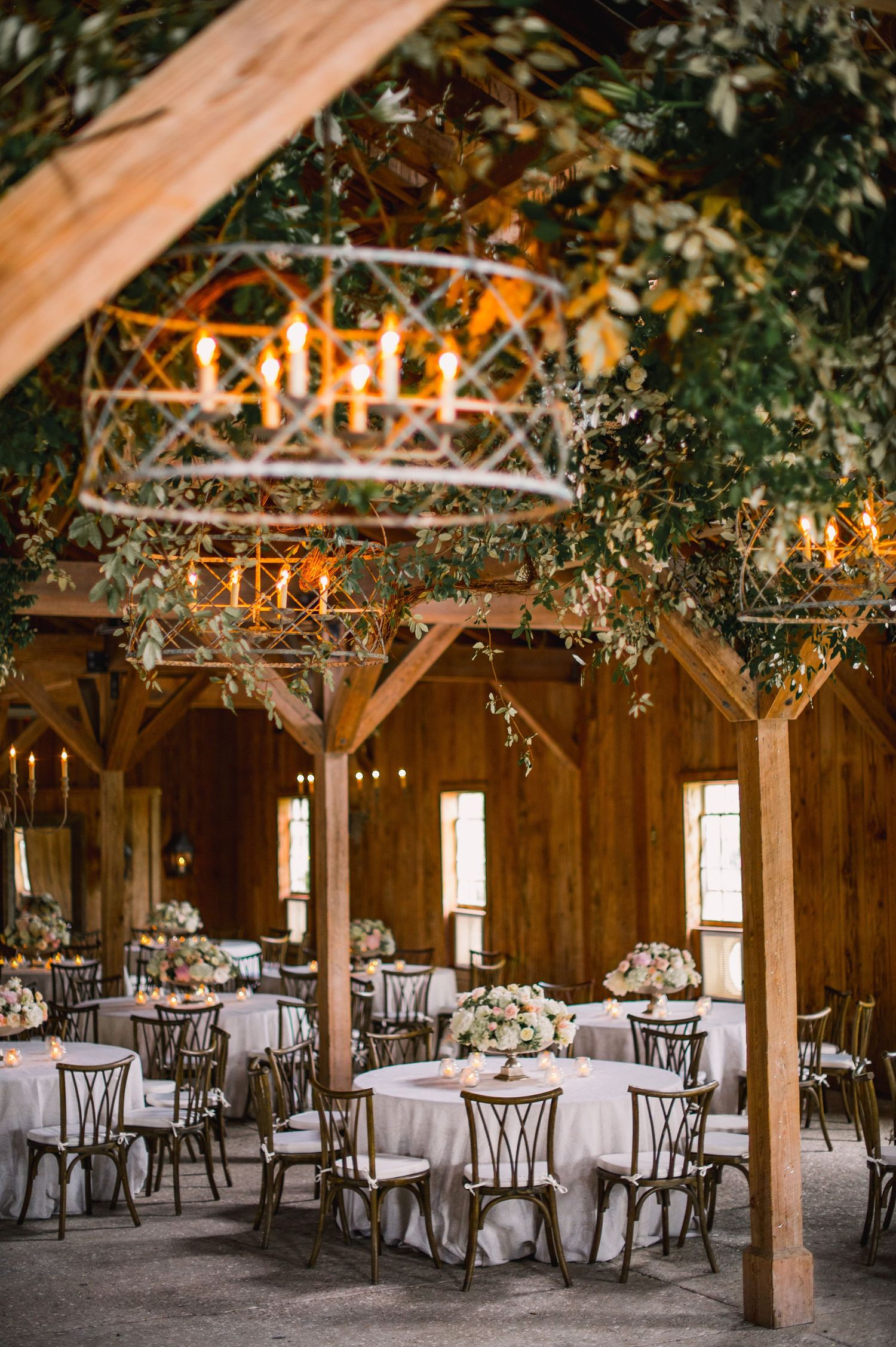 Rustic barn wedding reception venue decorated with twinkling lights and greenery hanging from wooden beams.