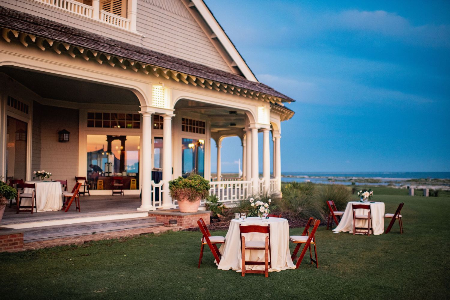 A panoramic view of a luxurious estate with white columns and wrap-around porch overlooking scenic countryside.