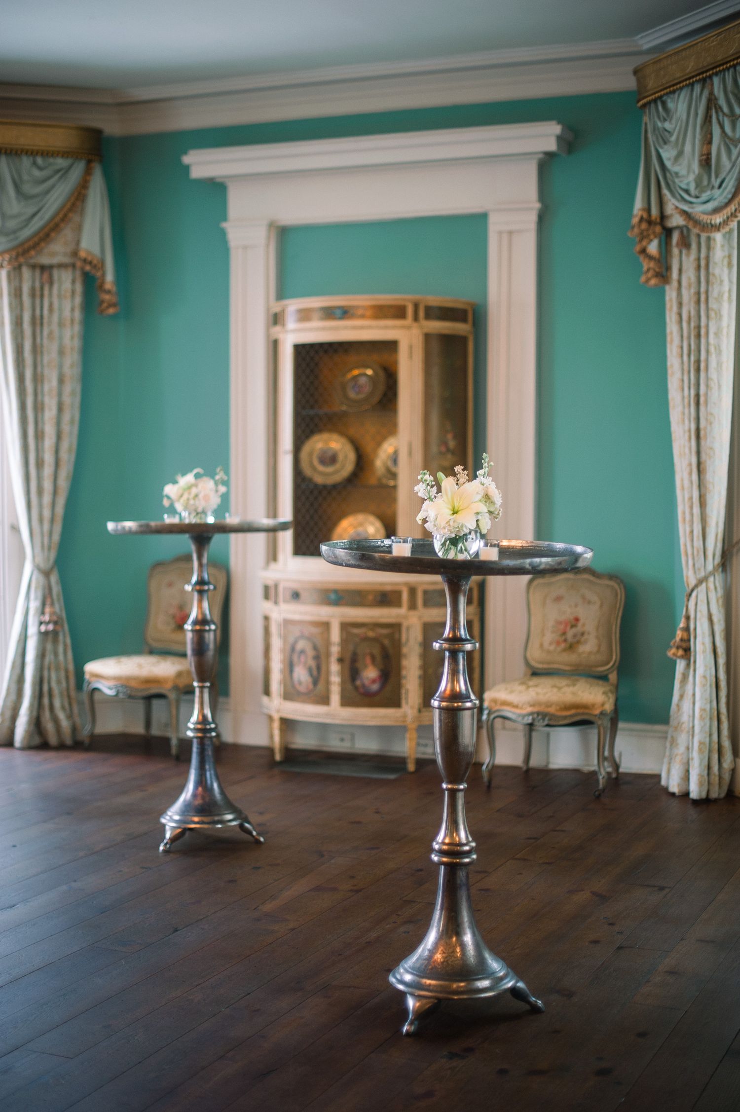 Elegant dining room with turquoise walls, white trim, and ornate gold curtains features multiple round tables with candelabras.