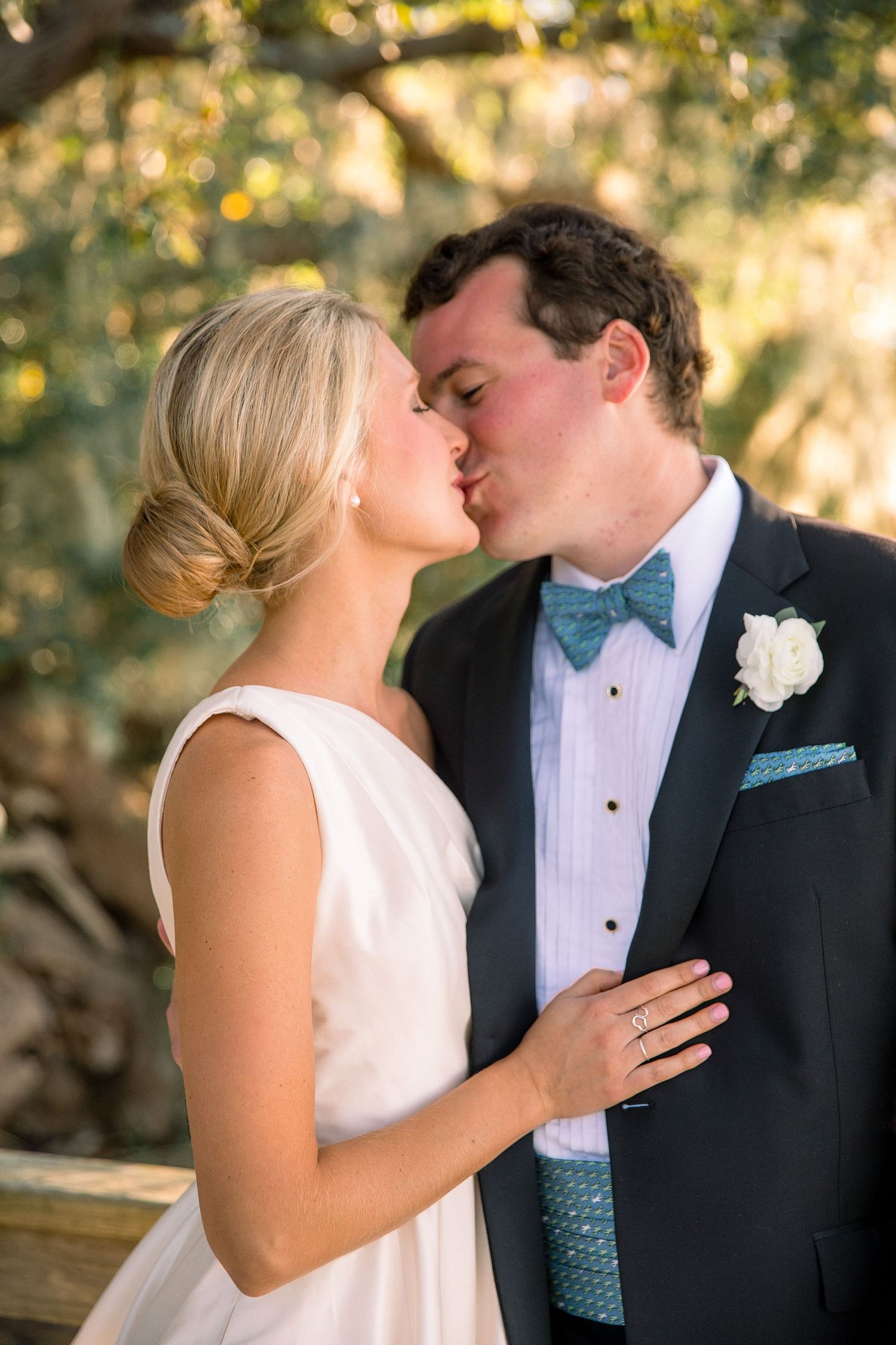 A bride and groom share a romantic kiss outdoors in formal wedding attire during their special day.