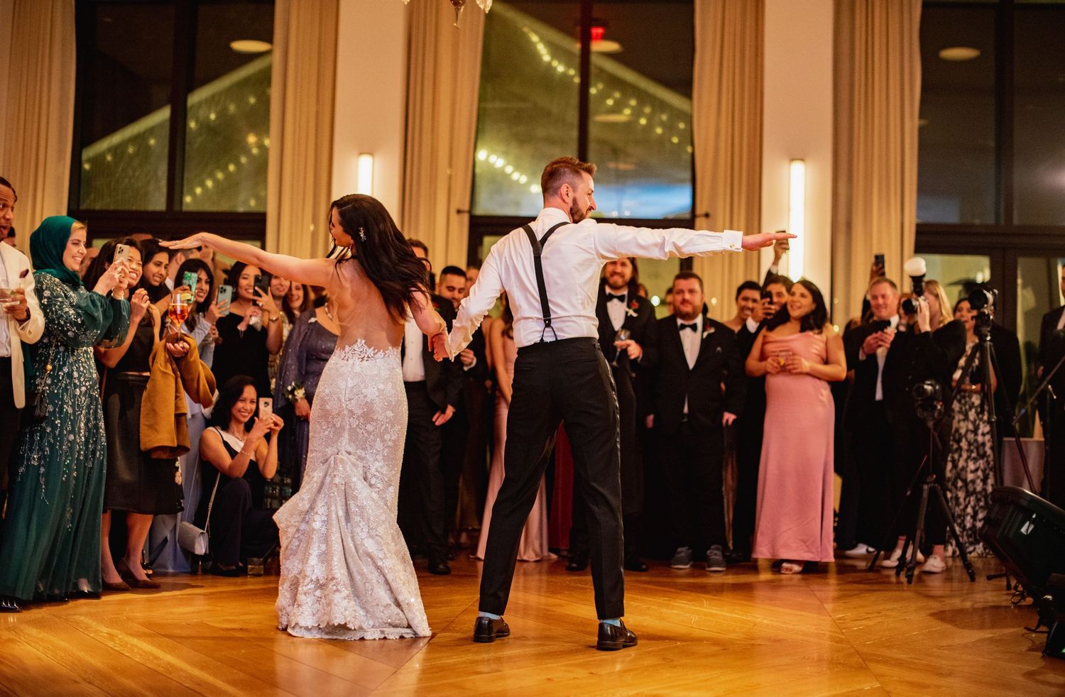 Wedding reception guests dance and celebrate on a wooden dance floor in an elegant ballroom setting.