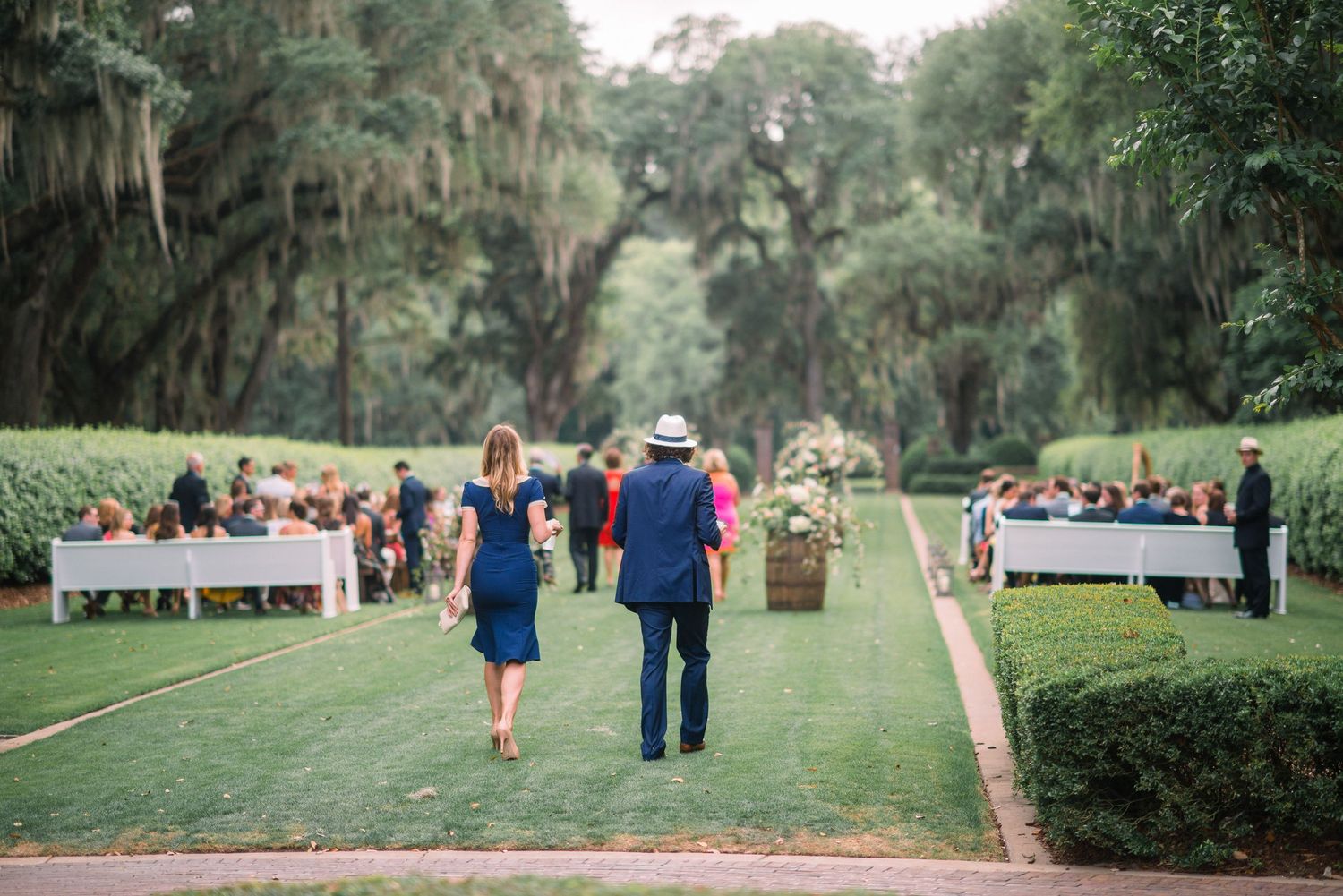 A scenic garden walkway with Spanish moss-draped oak trees and lush landscaping during a gathering.
