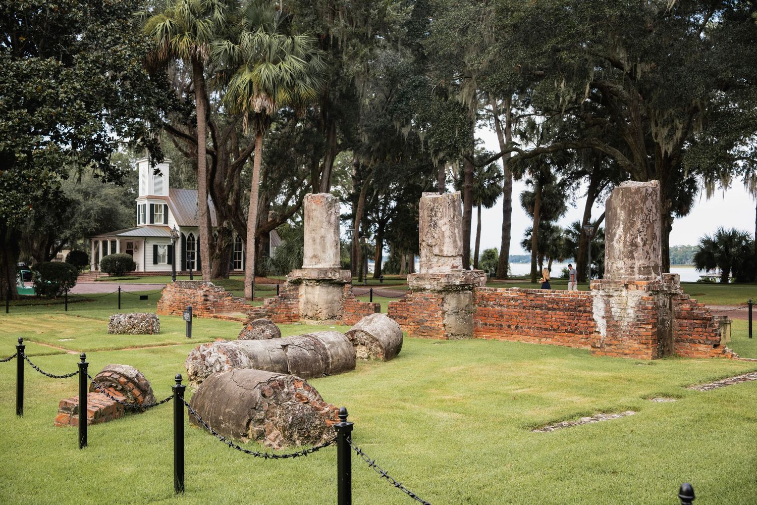 Historic cemetery ruins with stone walls and monuments surrounded by lush green grass and tall trees.