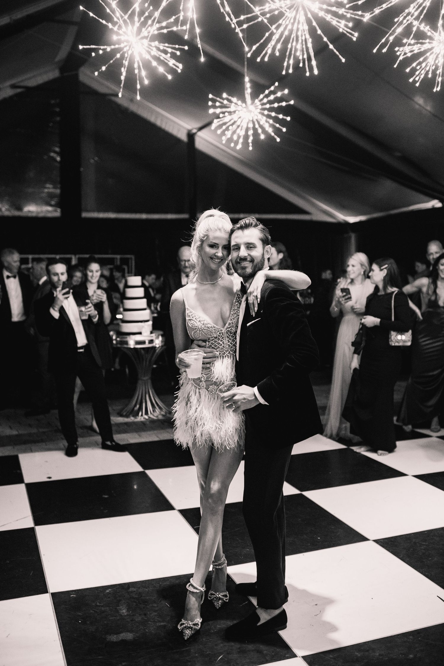 A couple dances on a black and white checkered floor under sparkling firework lights at an elegant party celebration.