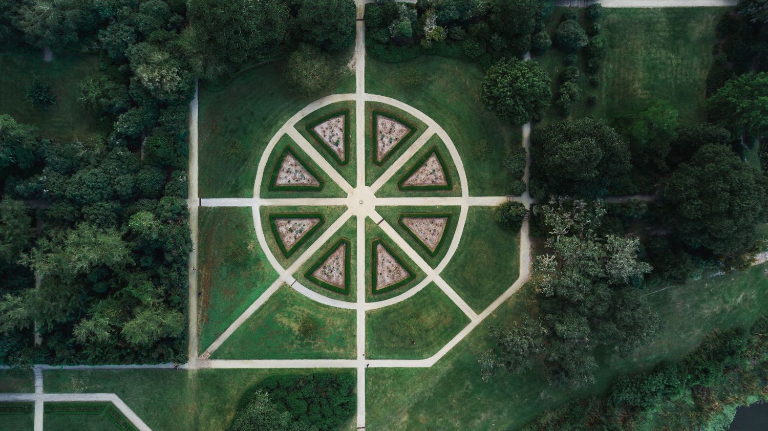 Aerial view of a green park with white geometric patterns and pathways creating a symmetrical design.