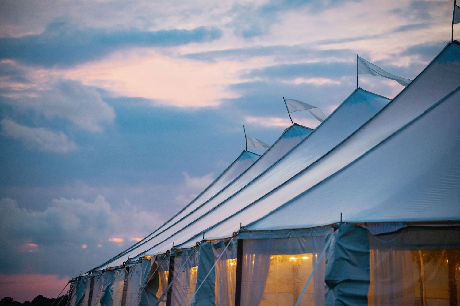 Row of white wedding tents silhouetted against a dramatic sunset sky.