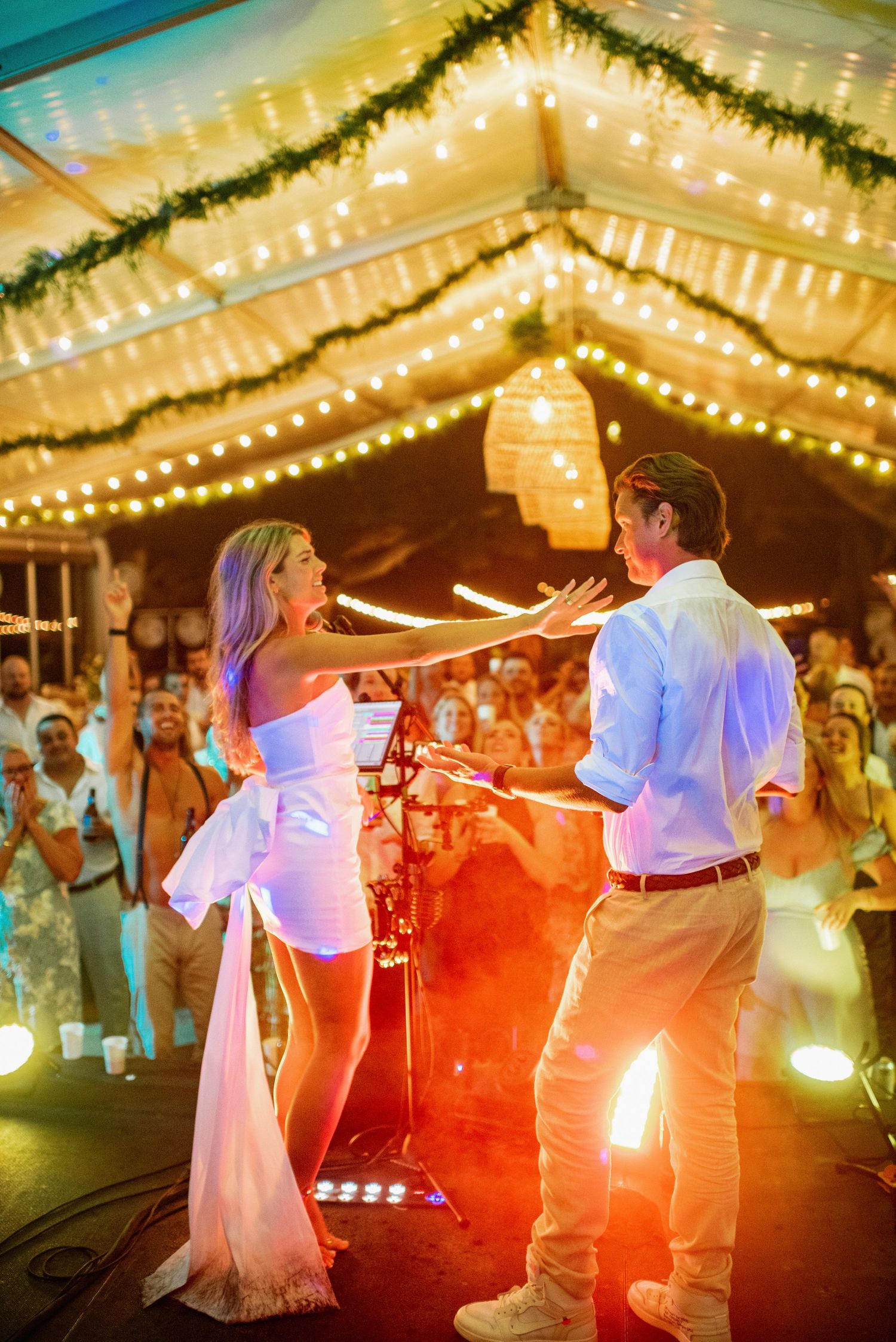 Couple dancing together under twinkling lights at a romantic wedding reception with colorful lighting effects.