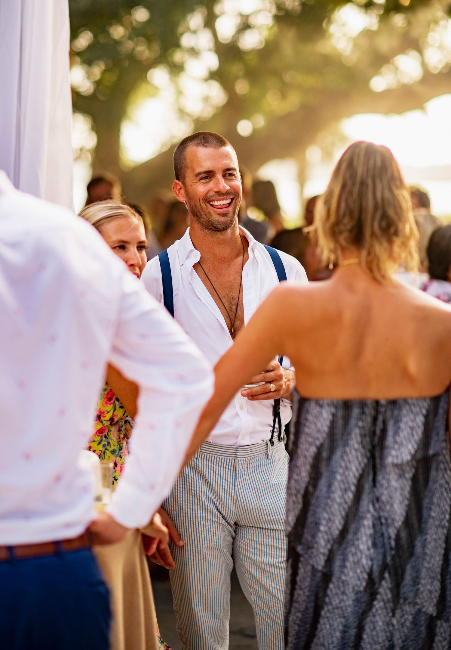 Wedding guests dancing and celebrating at an outdoor reception with bokeh lights in the background.