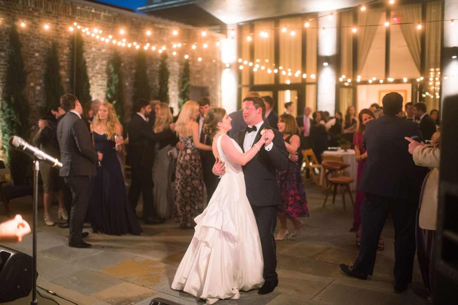 Couples dance at an elegant wedding reception with string lights and warm ambiance in an indoor venue.