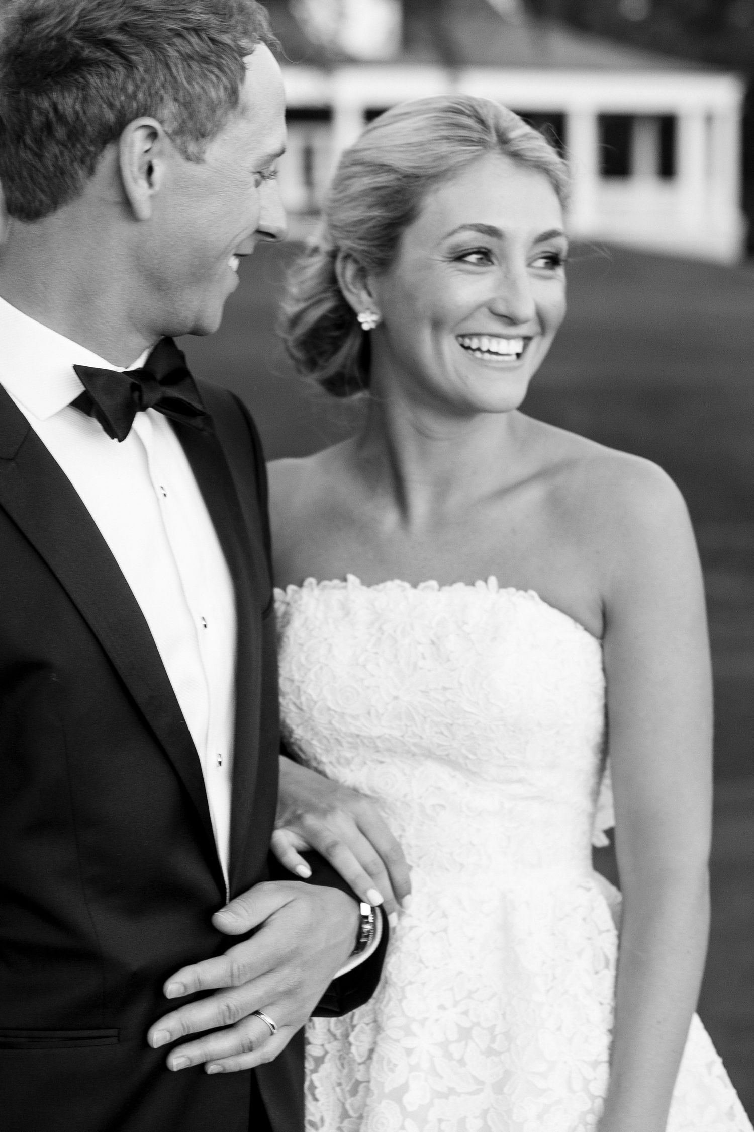 A black and white wedding portrait of a couple sharing a joyful moment in formal attire.