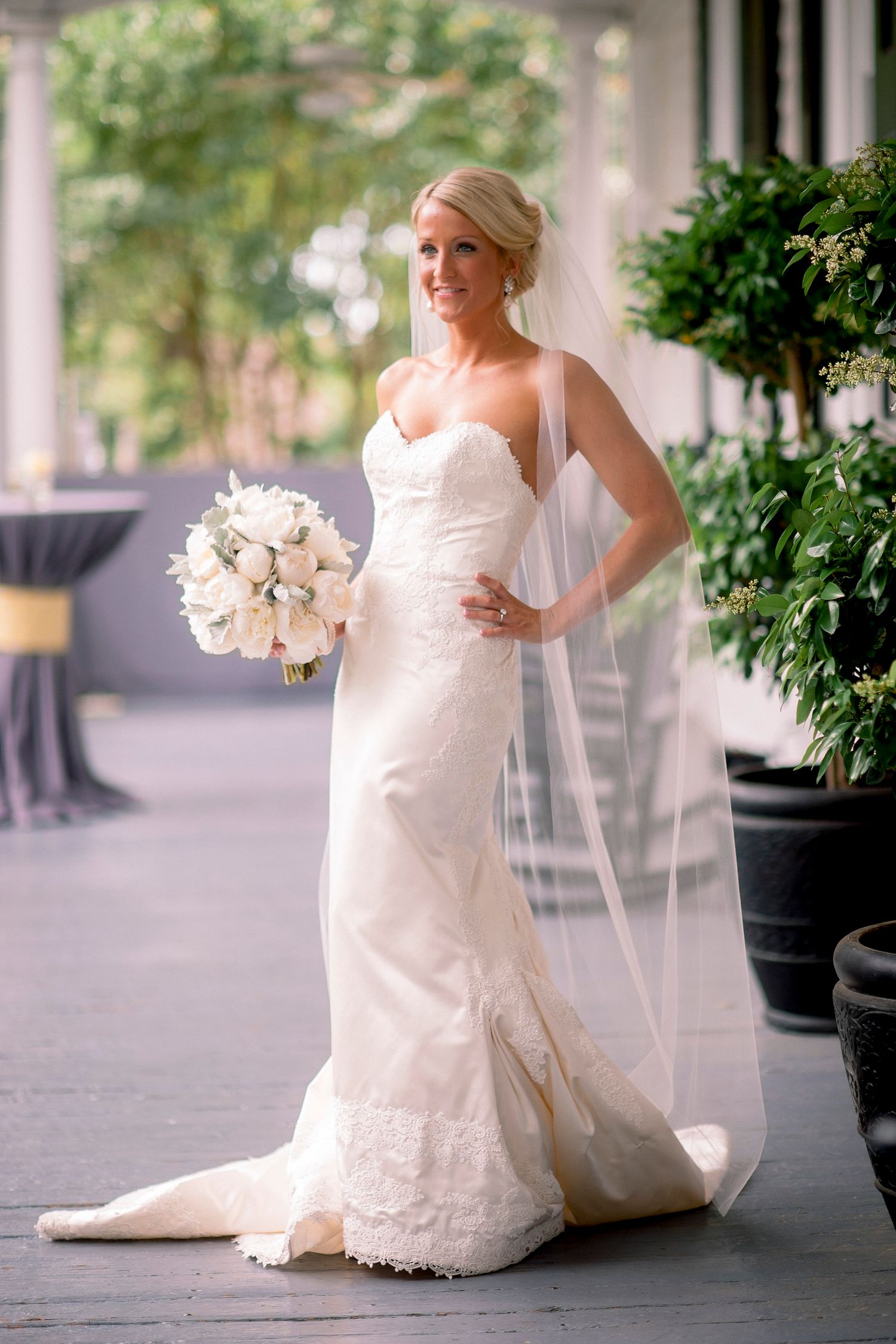 A bride in a white wedding gown poses elegantly in a series of photos along a city sidewalk with white bouquet.