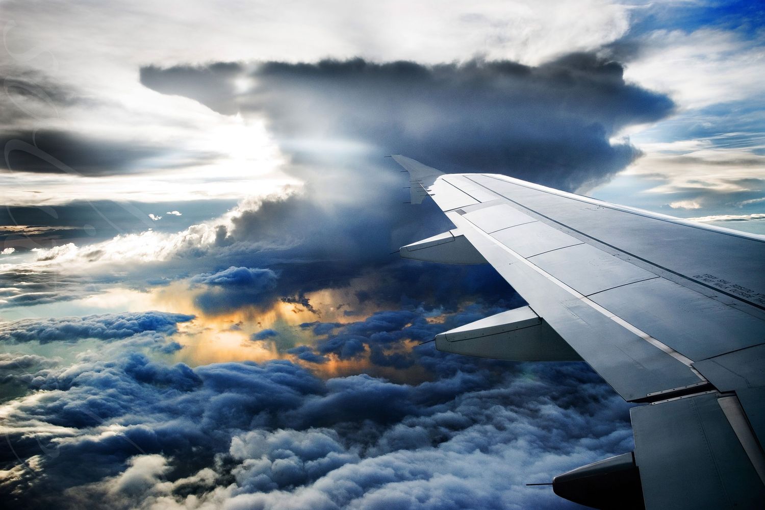 Dramatic view of airplane wing soaring through stormy clouds with sunlight breaking through.