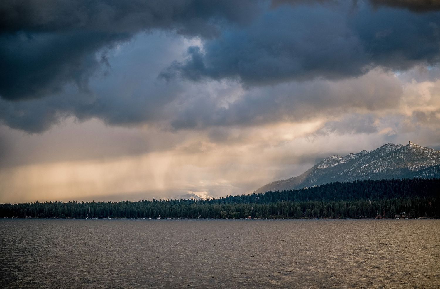 Dramatic stormy mountain landscape panorama with dark clouds and snow-capped peaks.
