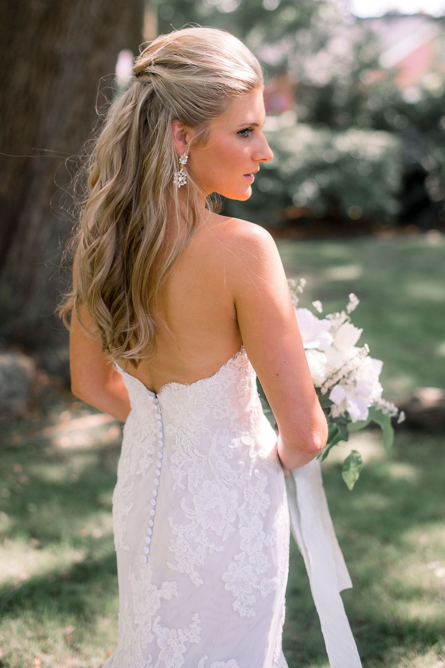 A bride in an elegant white strapless wedding gown poses in a garden setting.