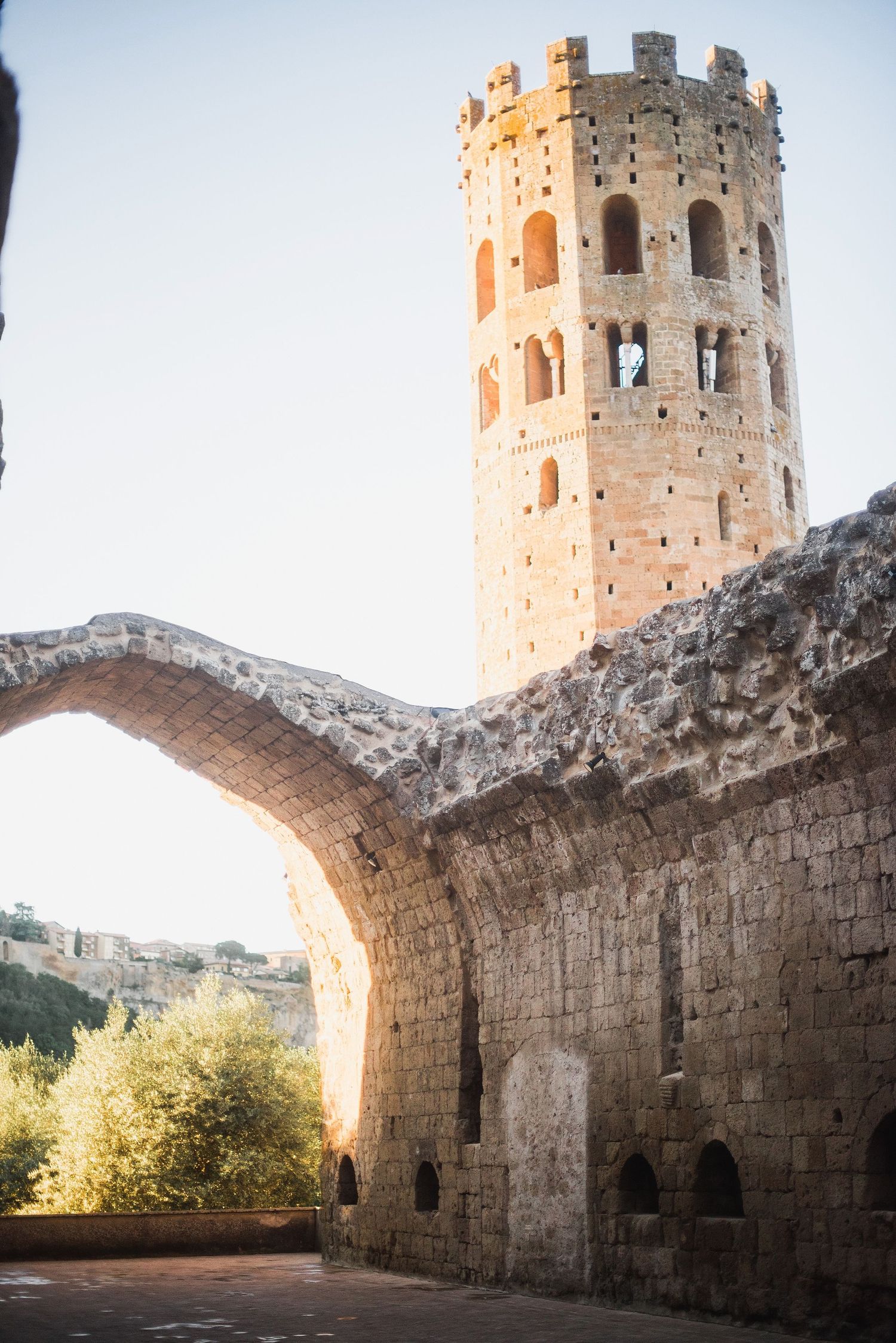 Ancient stone tower with crenellated top rises above an arched medieval passageway in Mediterranean architecture.