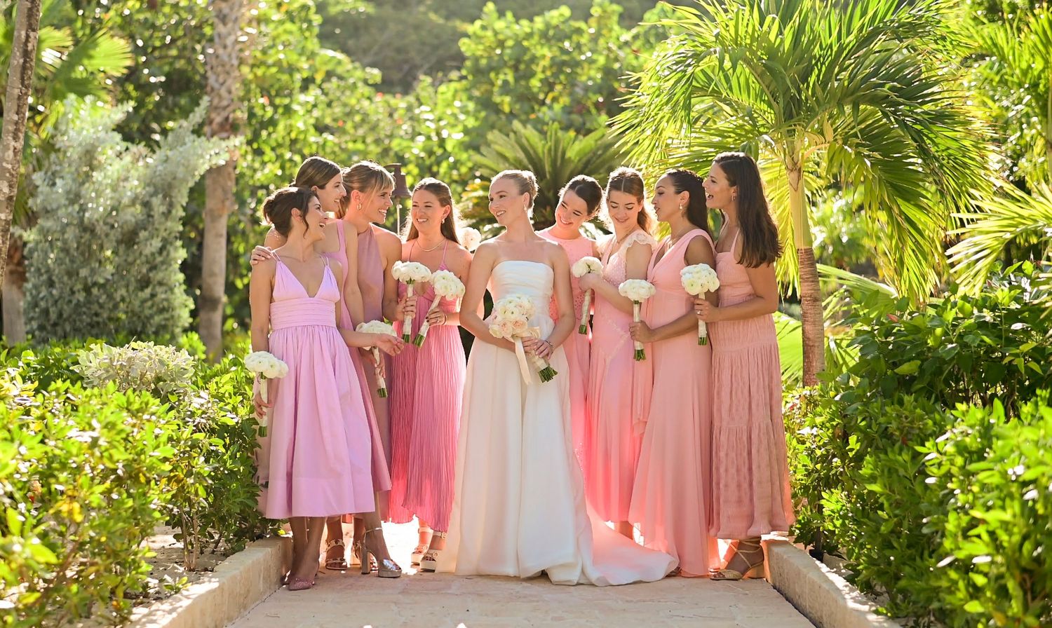 Wedding party lined up in pink and white dresses against a tropical garden backdrop.