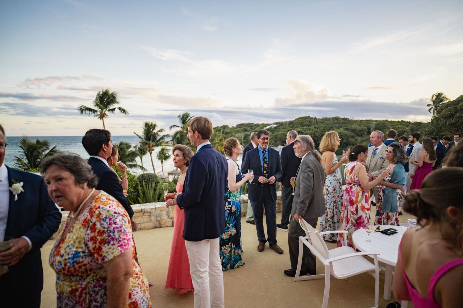 Wedding guests mingling at an outdoor cocktail reception by the beach at sunset.