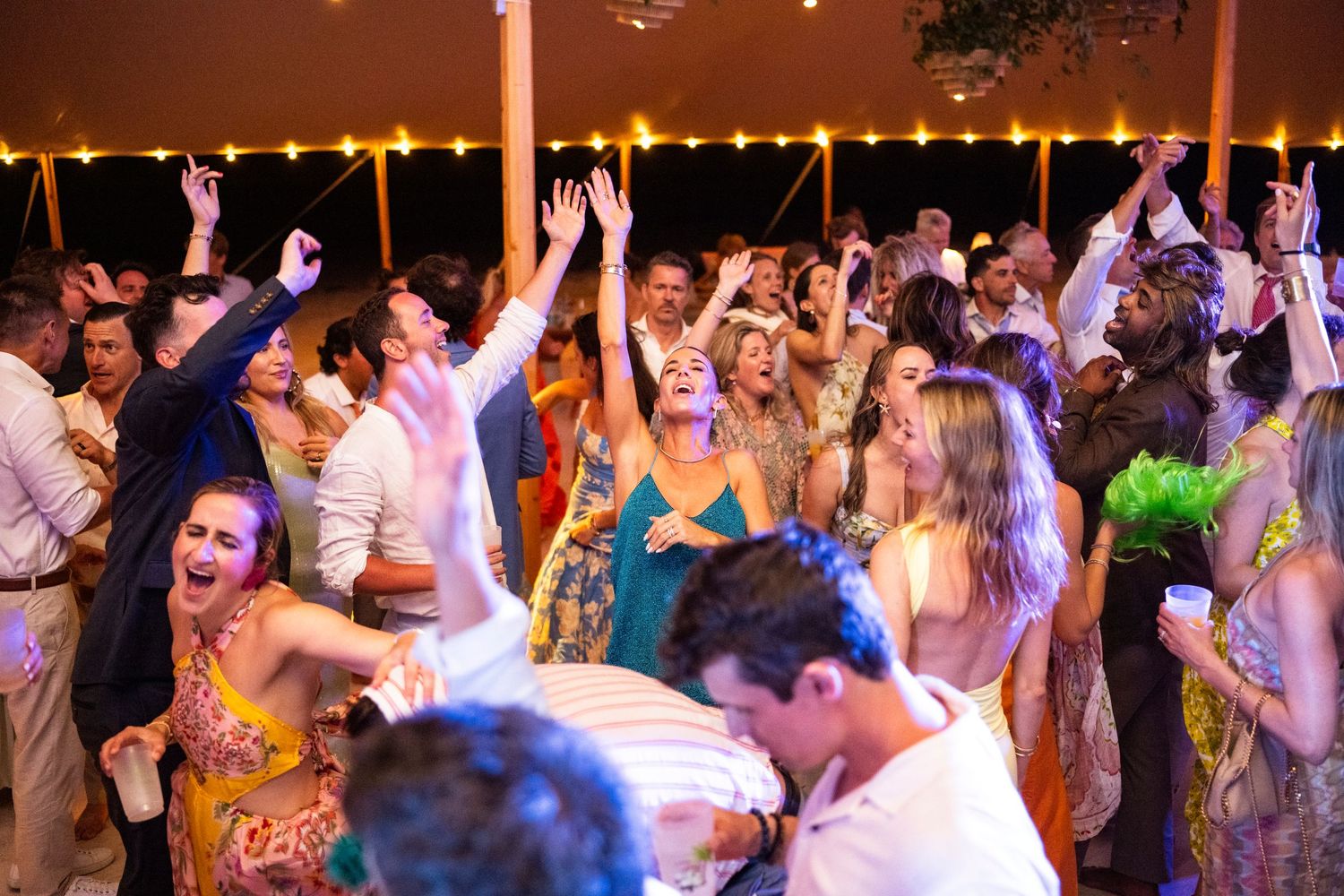 A crowded dance floor filled with energetic party-goers dancing under string lights at a festive celebration.