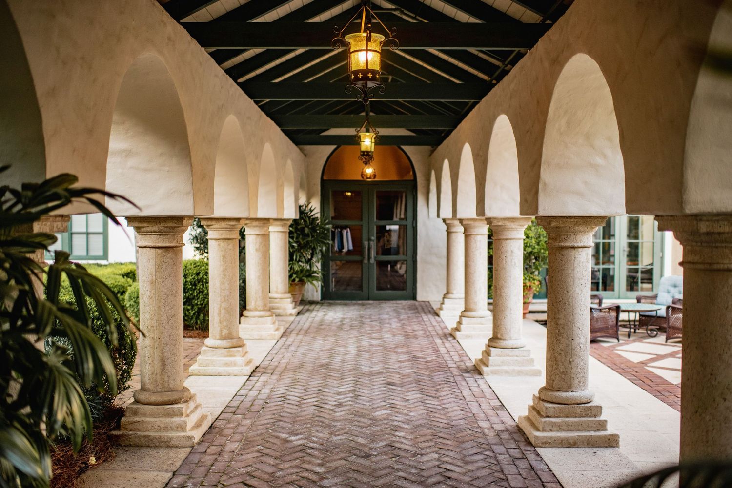 A series of arched stone columns line a covered walkway with Spanish colonial architecture and terracotta floors.
