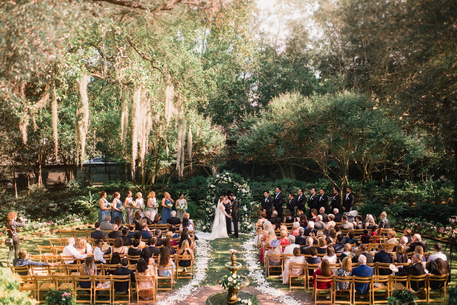 Panoramic view of an outdoor wedding ceremony in a lush forest setting with wooden chairs and floral decorations.