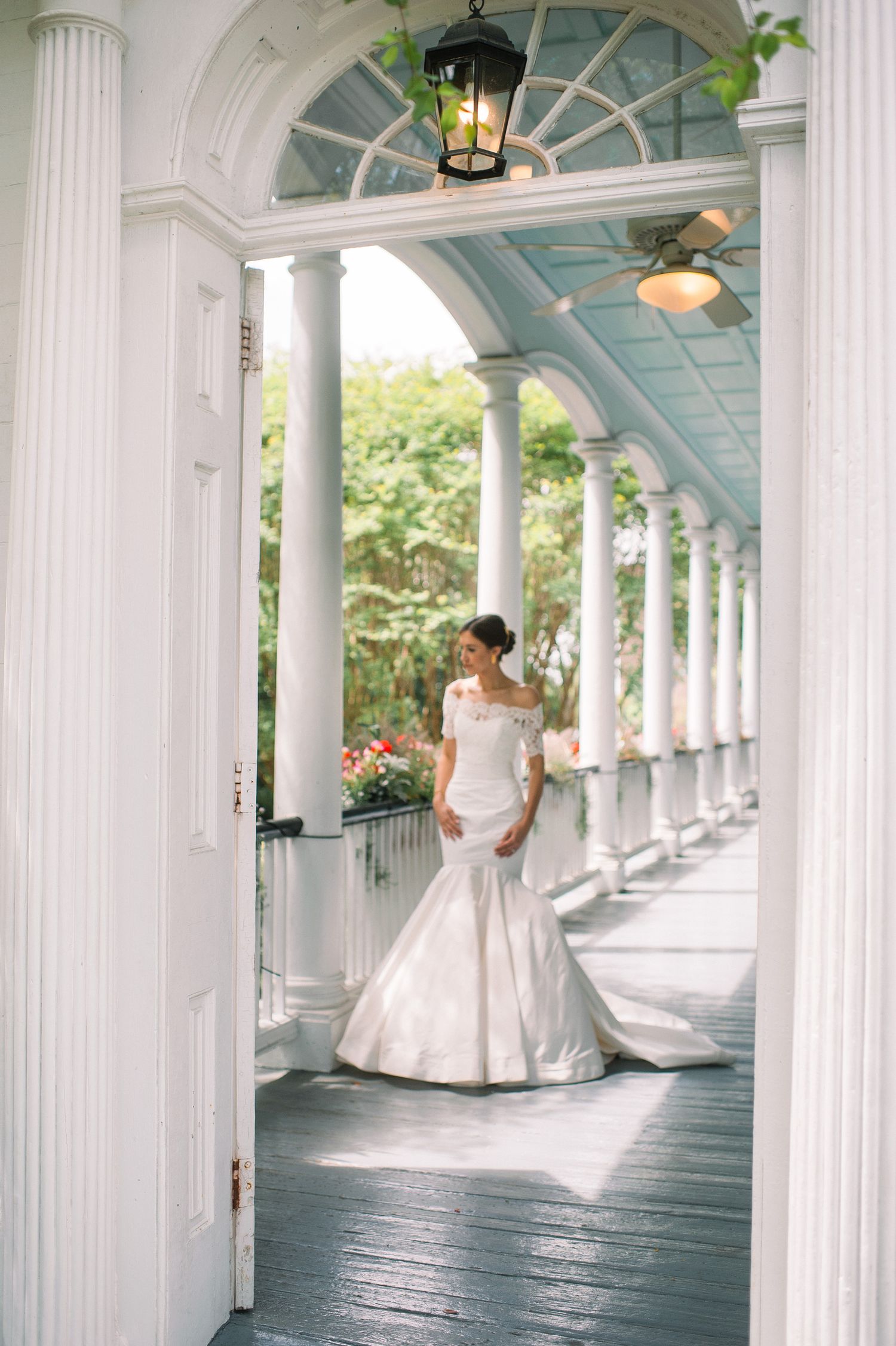 Elegant white wedding gown photographed on a classic Southern mansion porch with white columns and blue ceiling.