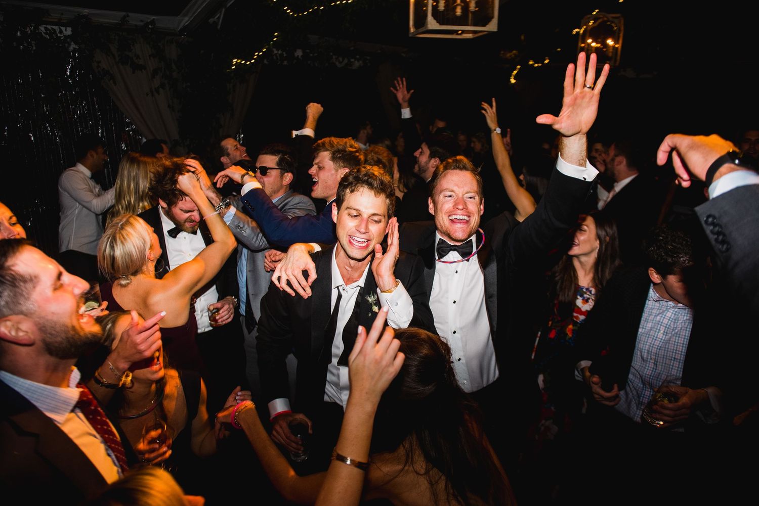 A group of people dancing and celebrating at a lively nightclub or party with dark atmospheric lighting.