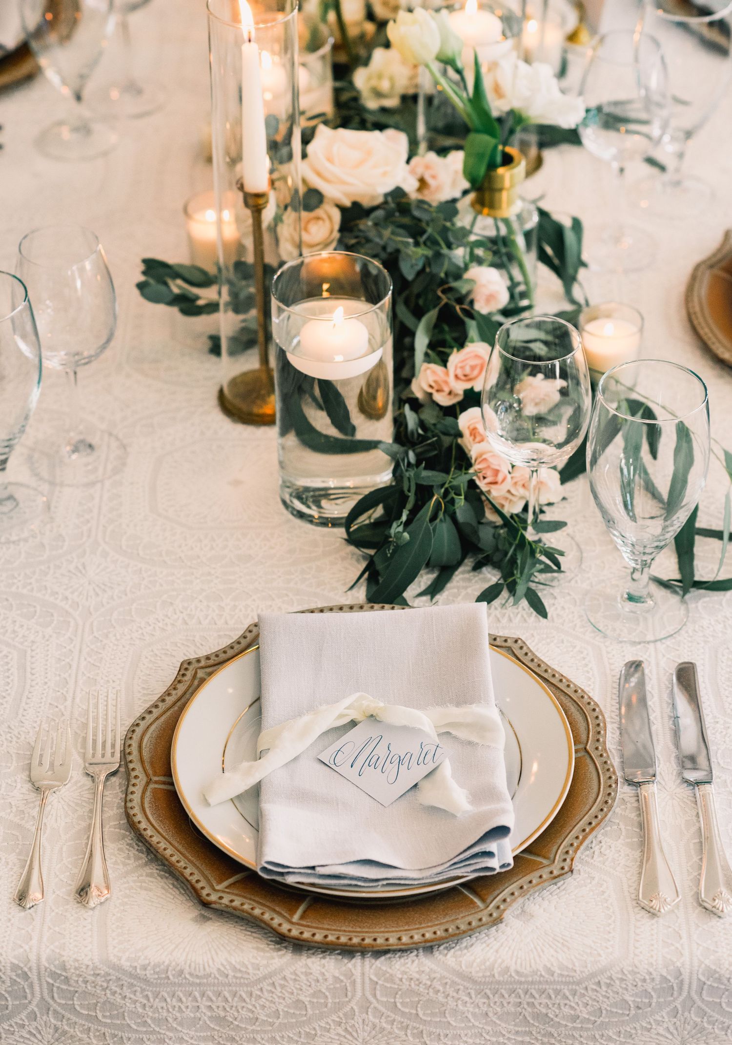 Elegant wedding table setting with gold chargers, white linens, and delicate floral arrangements in soft peach tones.