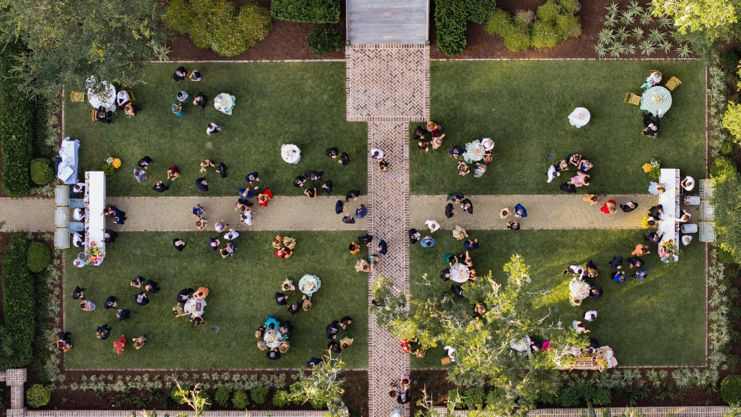 Aerial view of people gathered in an outdoor garden area with white decorative elements and landscaping features.