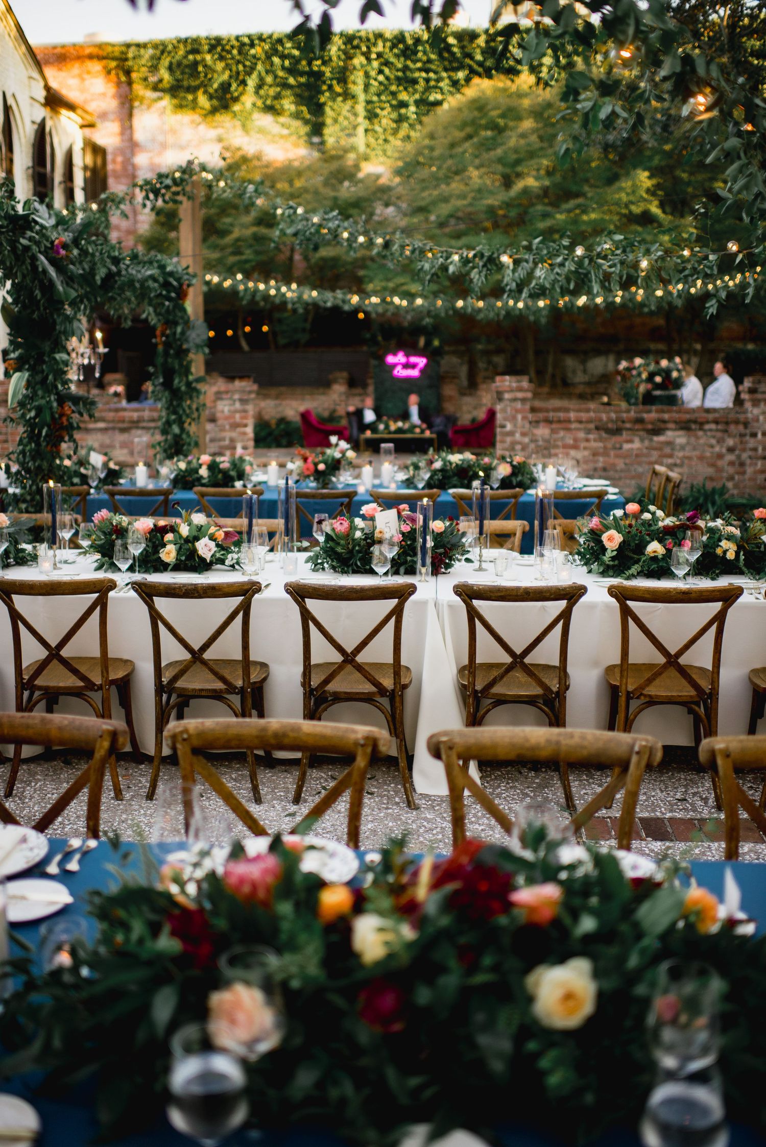Rustic wooden cross-back chairs lined up at an outdoor wedding reception with string lights and floral garlands.