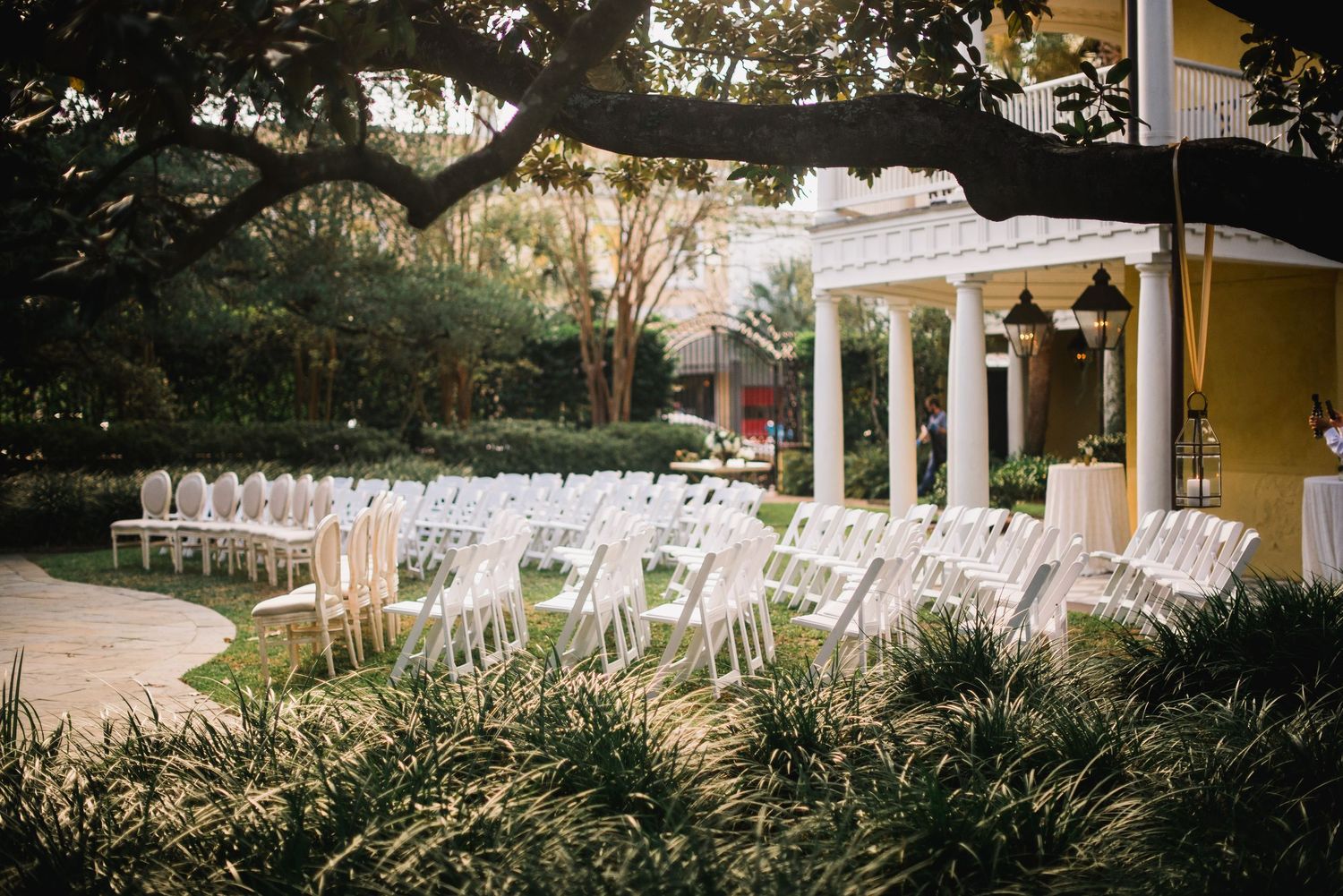 White chairs arranged in rows for an outdoor wedding ceremony with trees and a gazebo in the background.
