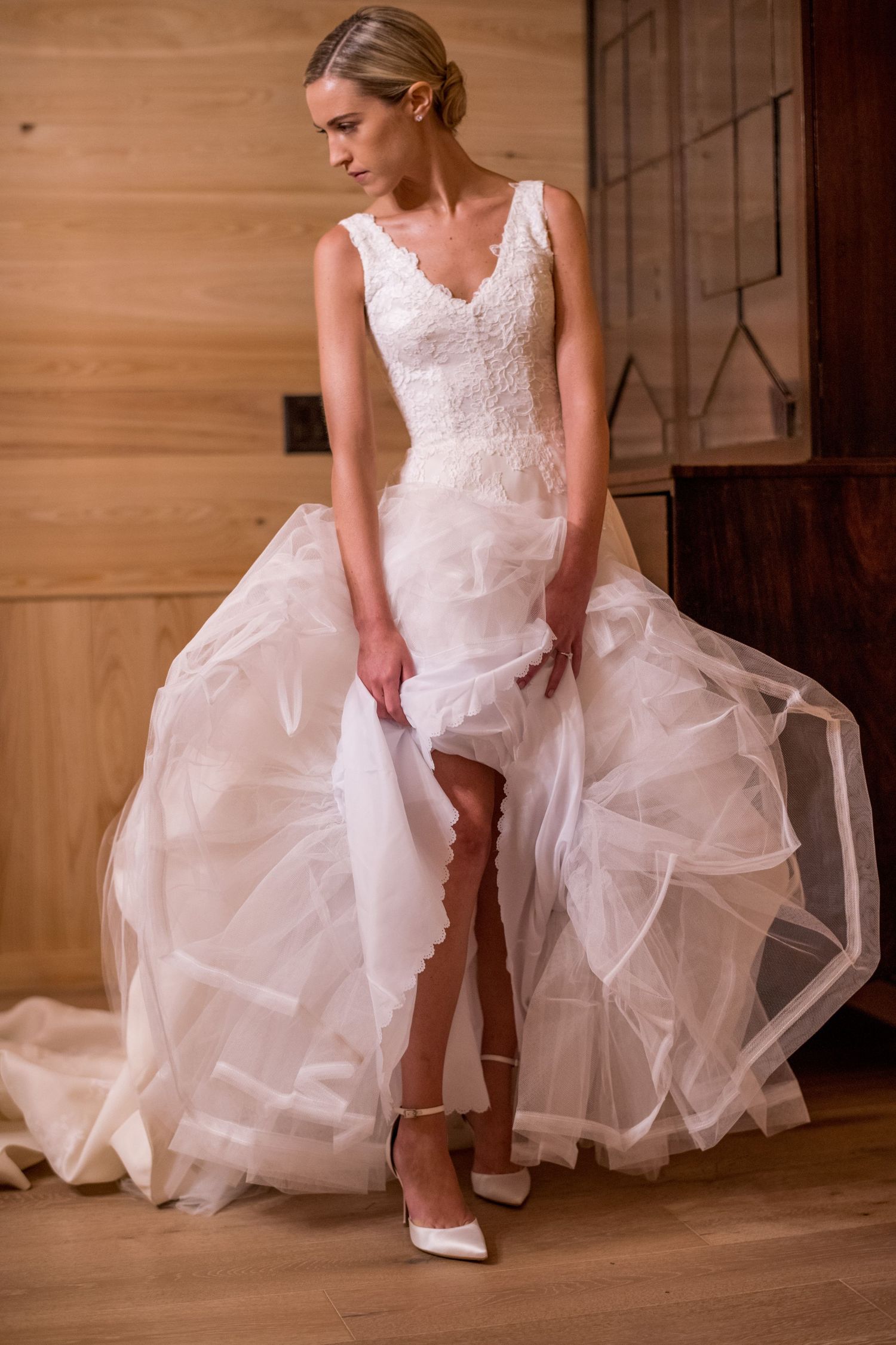 A bride in a white wedding dress and cowboy boots poses in a rustic setting, showing off her country-western style.