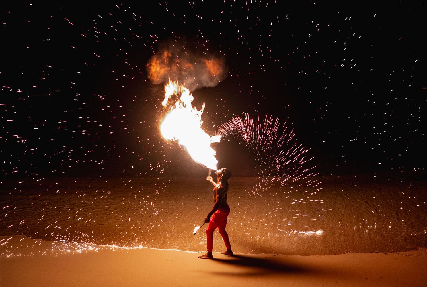 A series of fire performers twirling flaming batons against a dark night sky creating dramatic light trails and sparks.