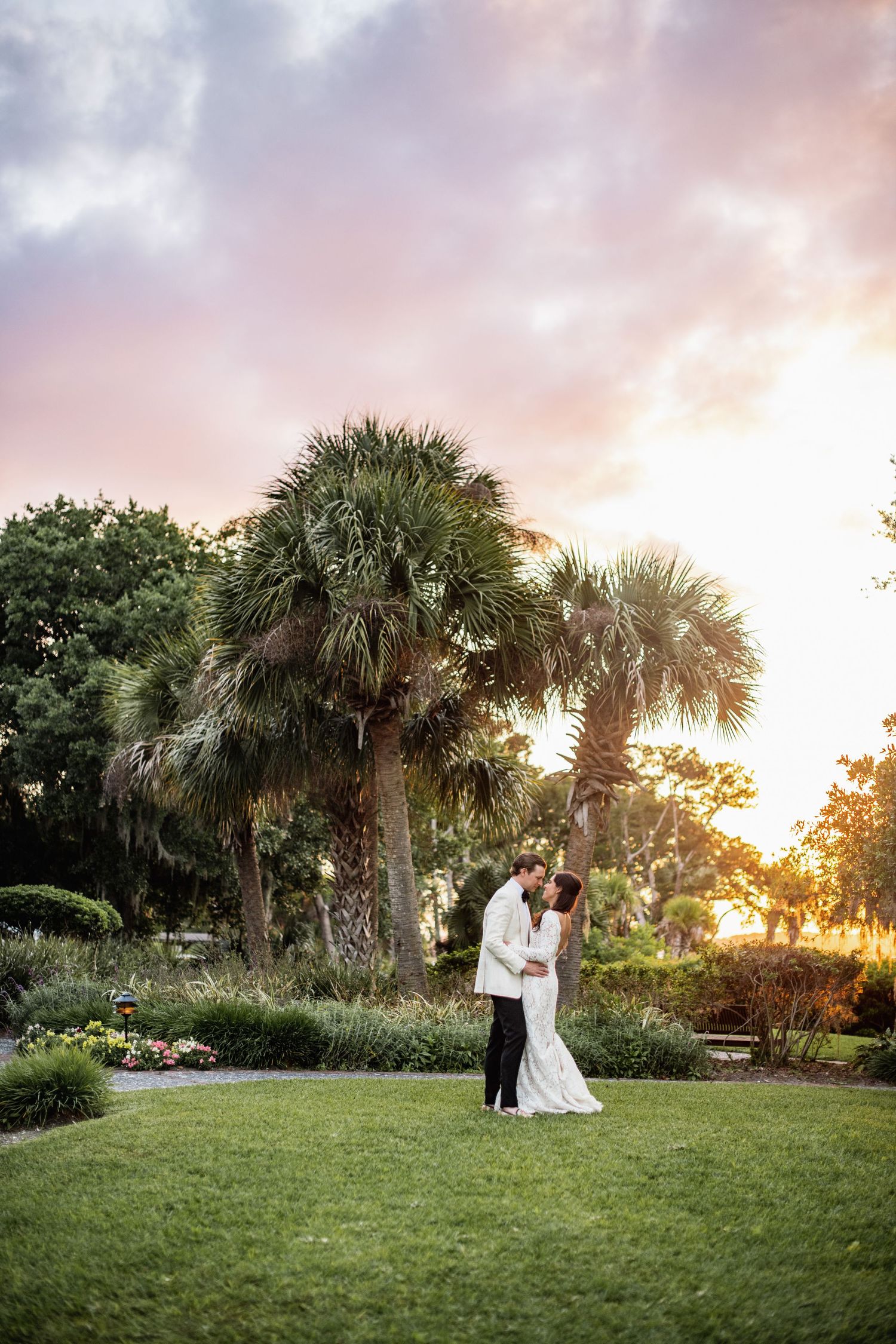 Wedding couple shares intimate moments at sunset in a tropical garden with palm trees.