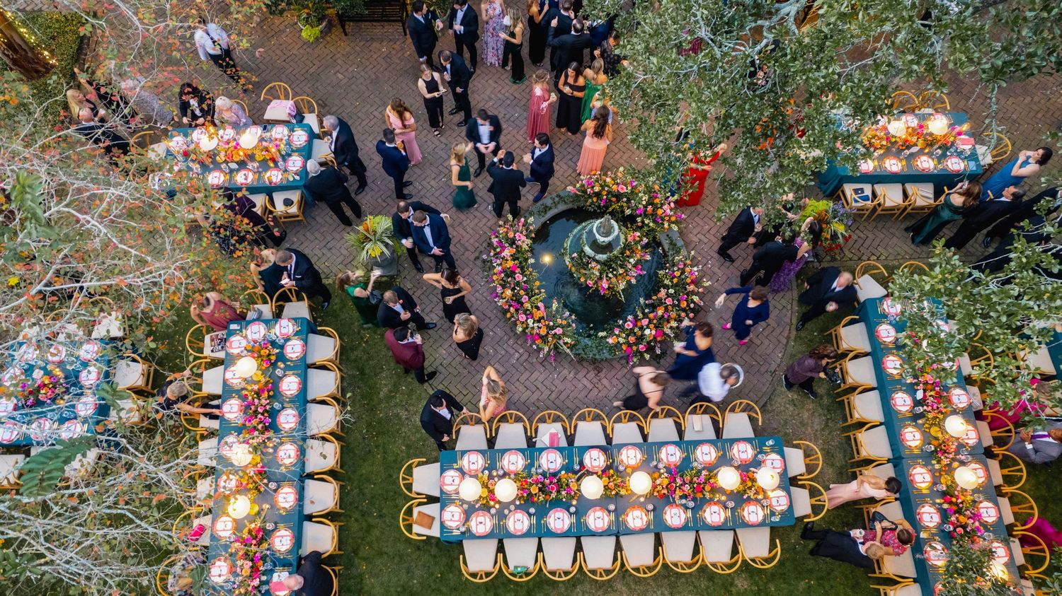 Aerial view of an outdoor event with rows of white chairs and orange decorations arranged in a garden setting.