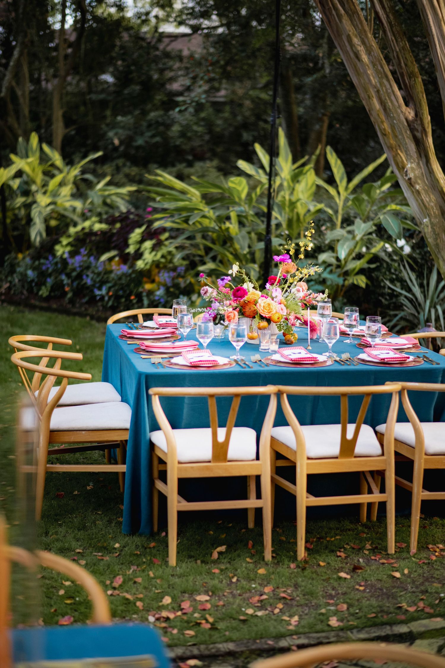 Outdoor garden party table setup with bright turquoise benches and colorful floral centerpieces for an elegant dining experience.