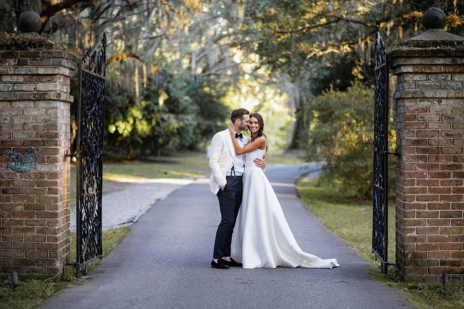 A couple in formal attire shares romantic moments along a tree-lined brick pathway during their wedding photoshoot.