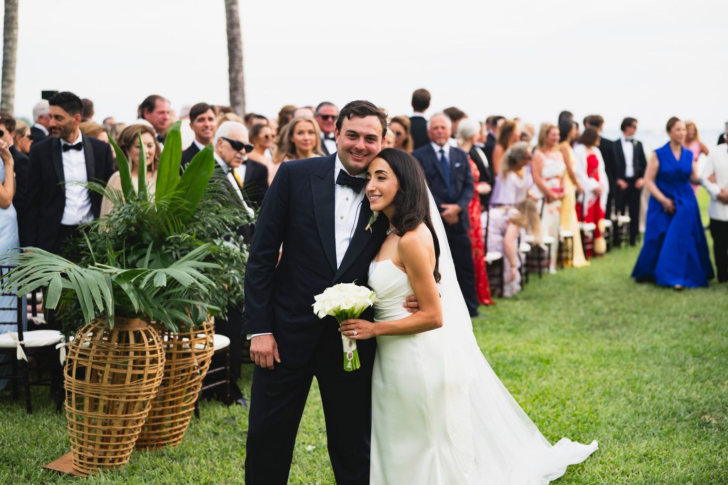 A bride and groom walk down the aisle at an outdoor garden wedding ceremony surrounded by guests.