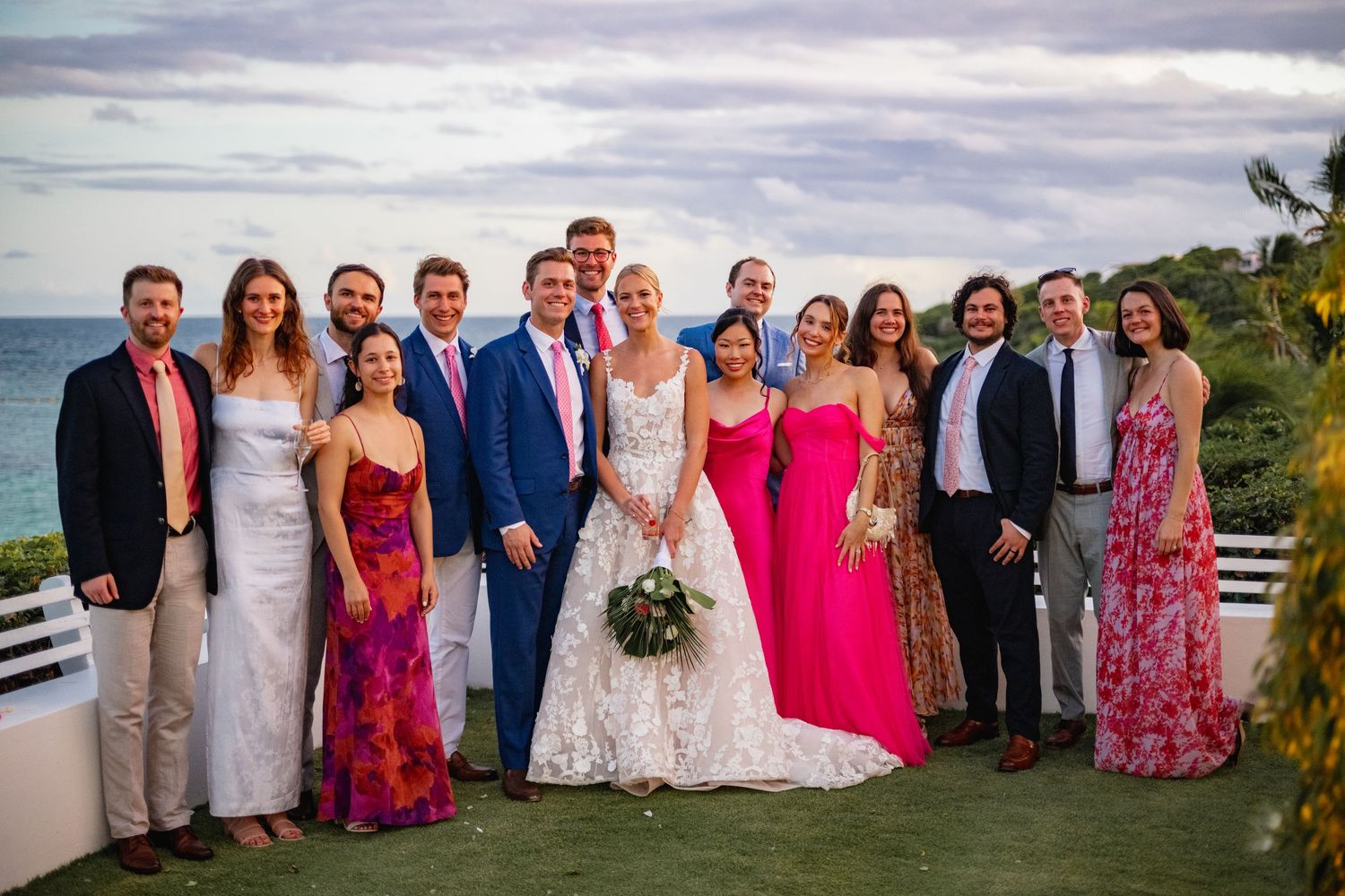Wedding party group photos on a beach with guests wearing colorful dresses and formal attire.